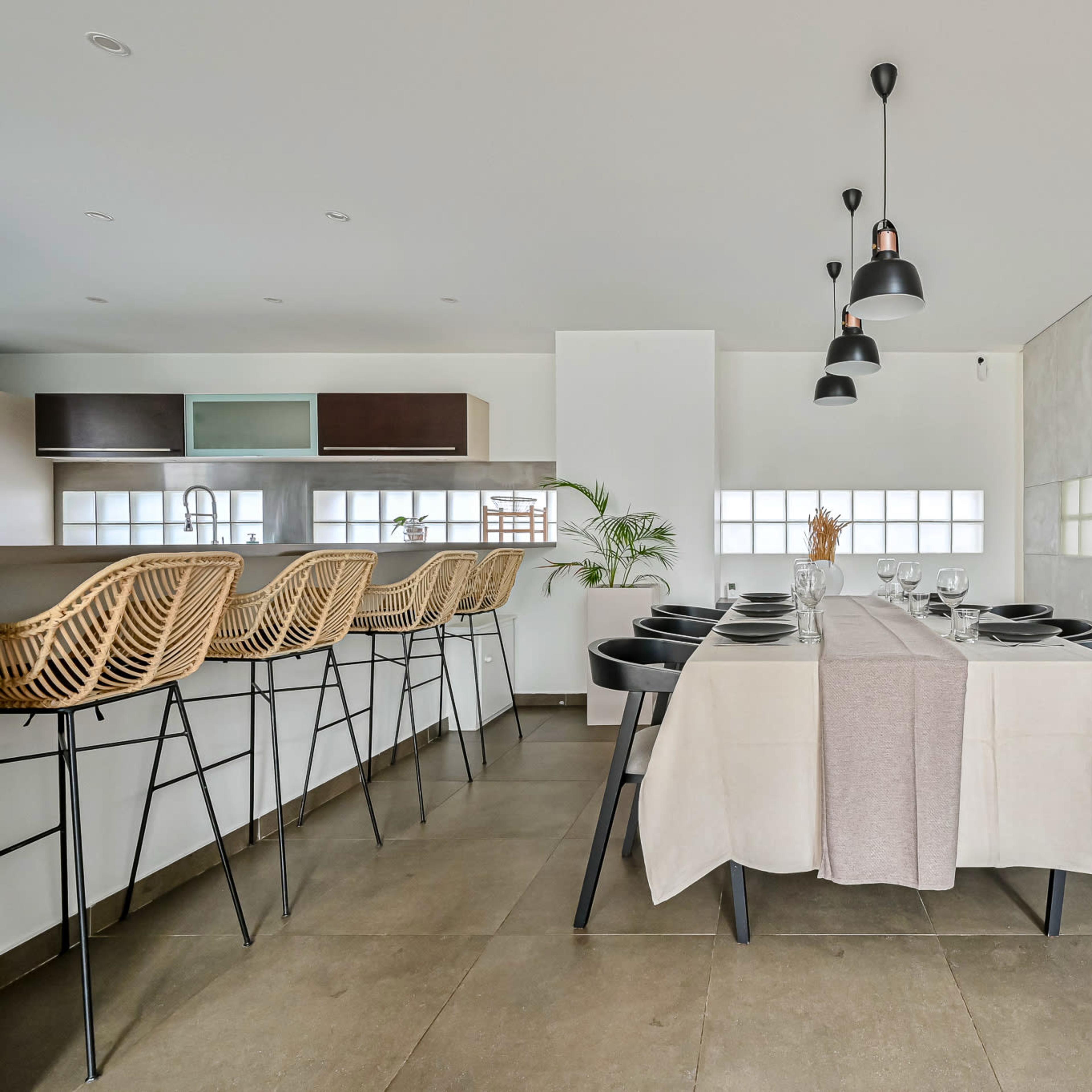 A modern dining area features a table set for a meal, with black chairs and pendant lighting overhead.