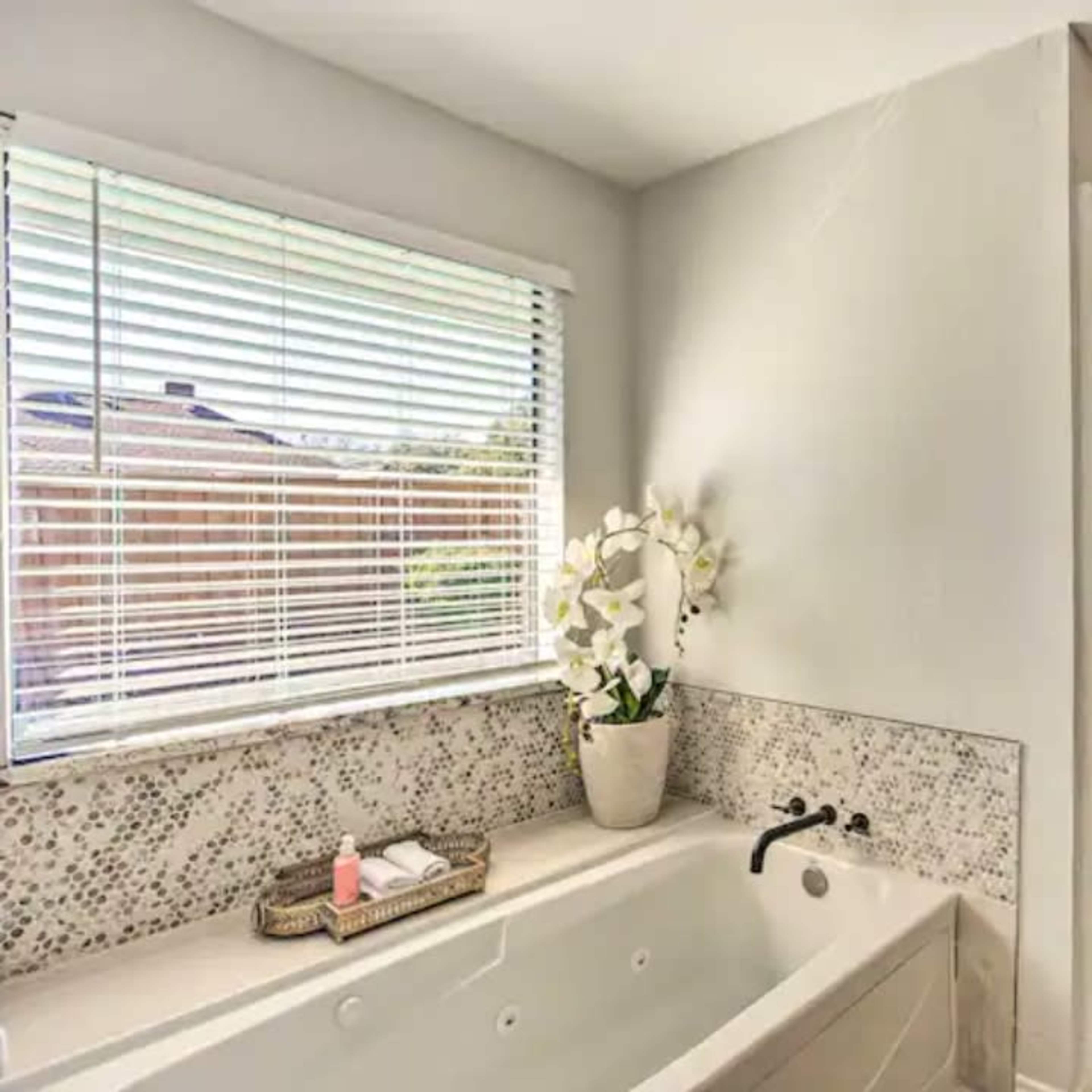 A modern bathroom featuring a large bathtub beside a glass shower enclosure and a window with blinds.