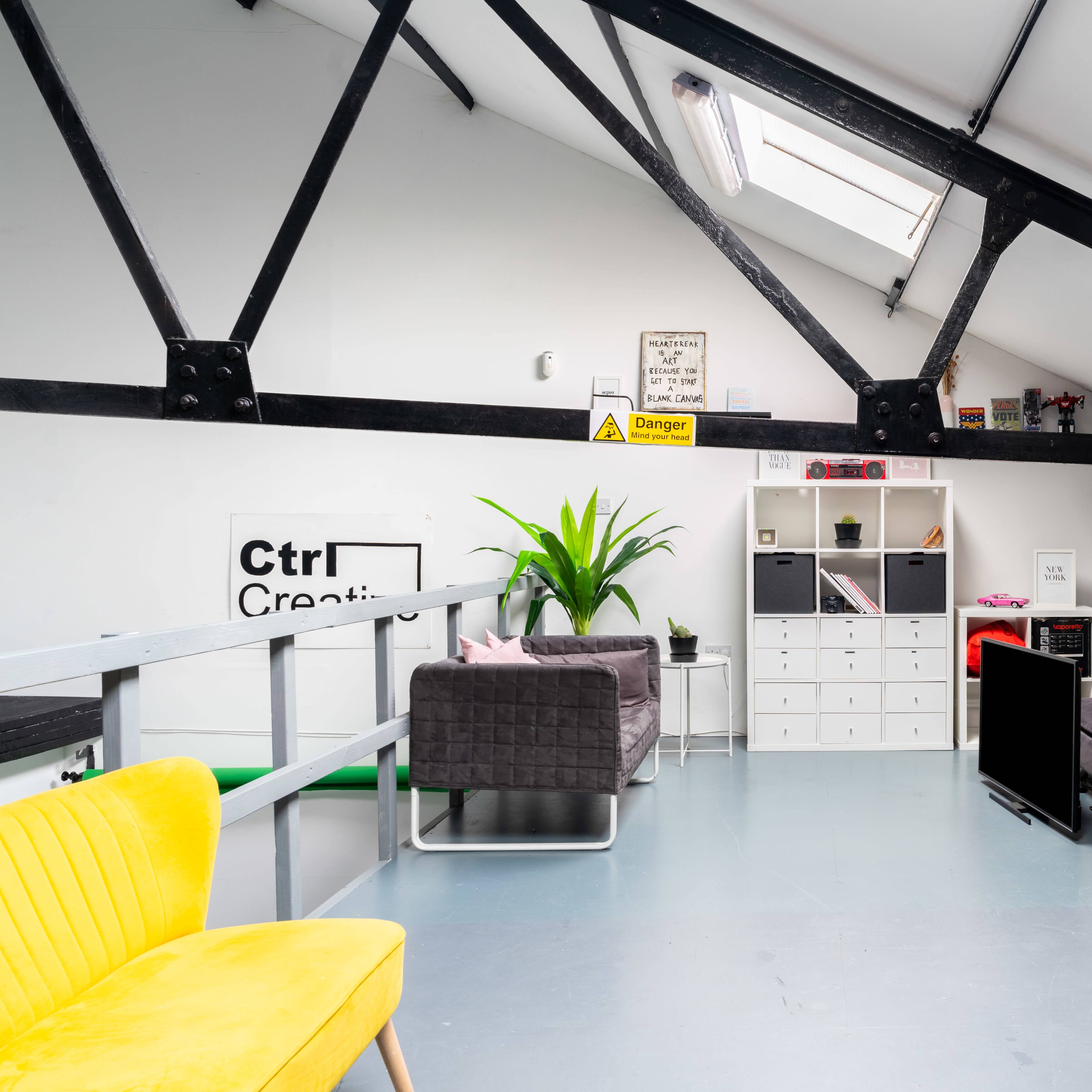 A modern loft-style workspace with a seating area, a white storage unit, and a small kitchenette under a skylight.