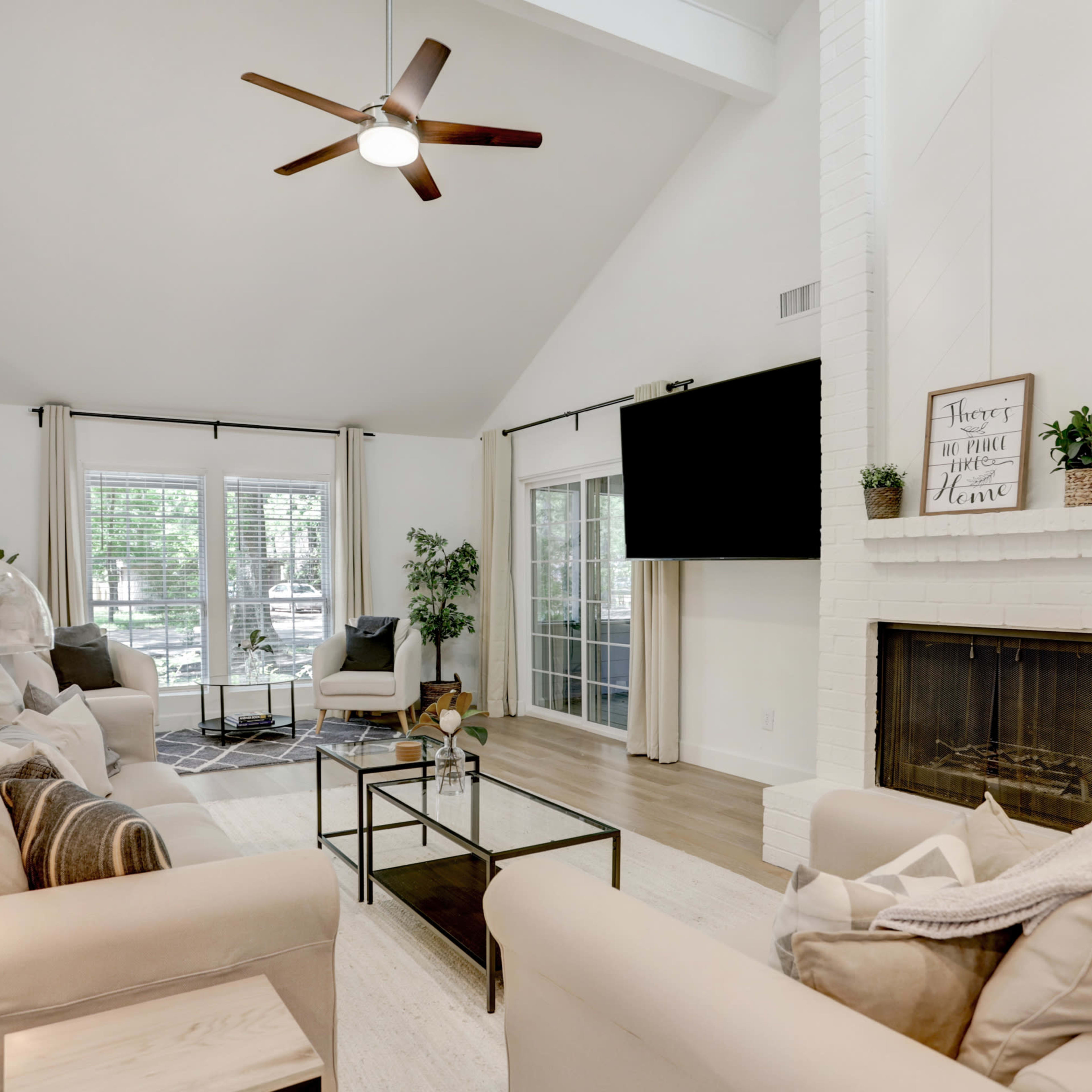 A modern living room with light-colored sofas, a glass coffee table, a fireplace, and large windows that let in natural light.