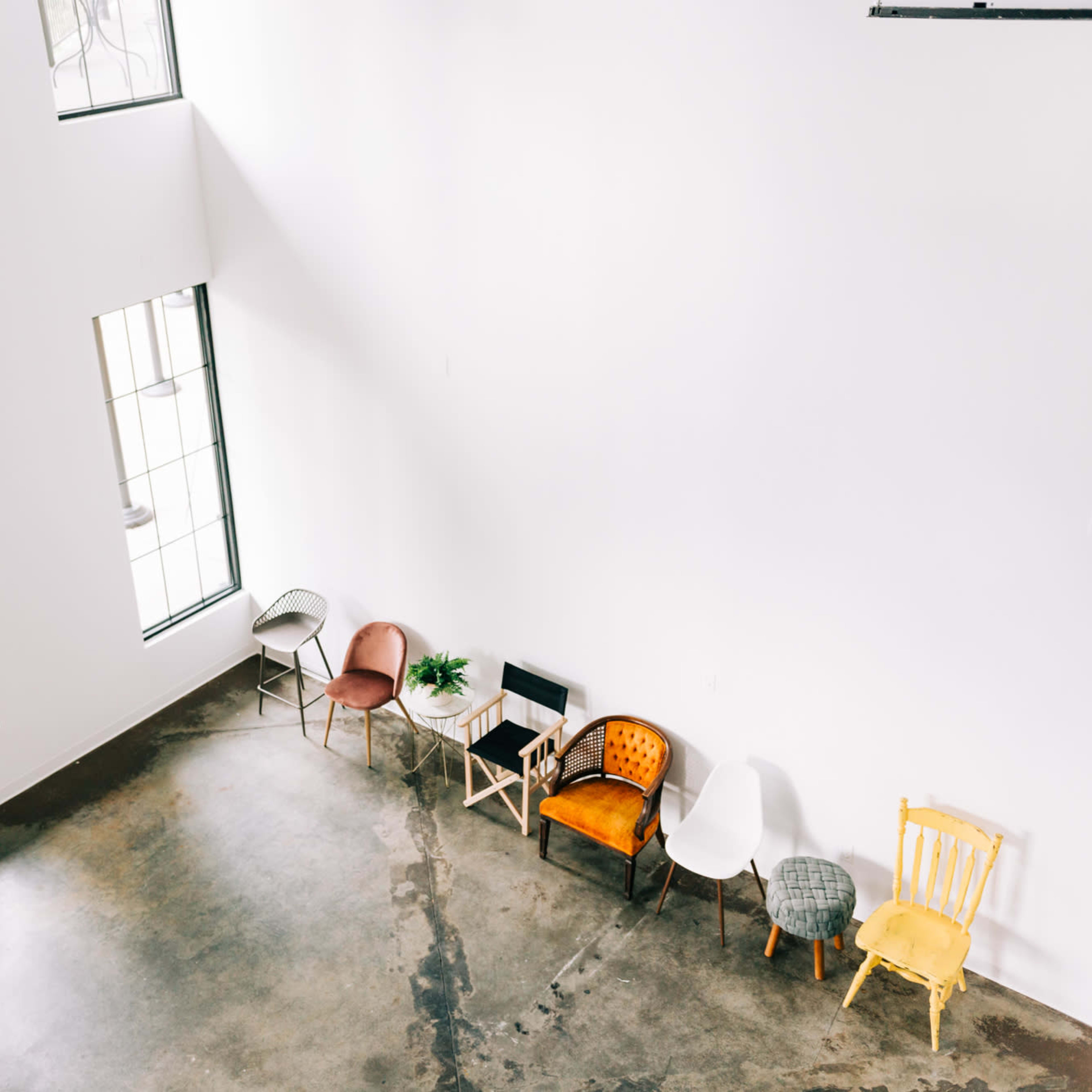 A spacious, well-lit room with a polished concrete floor and several chairs arranged along a white wall beneath large windows.
