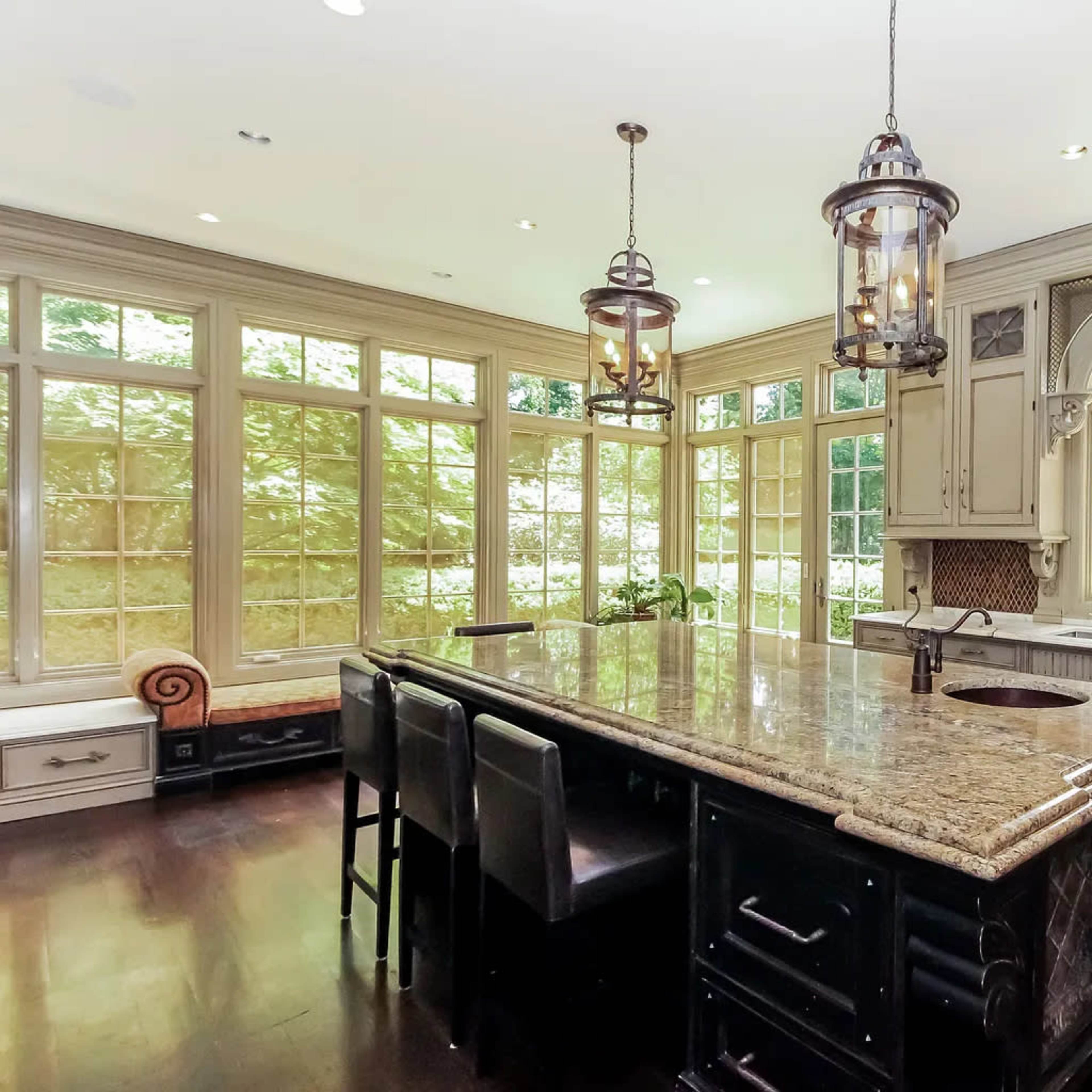 A spacious kitchen features a large granite island with seating, flanked by multiple windows allowing natural light to illuminate the room.