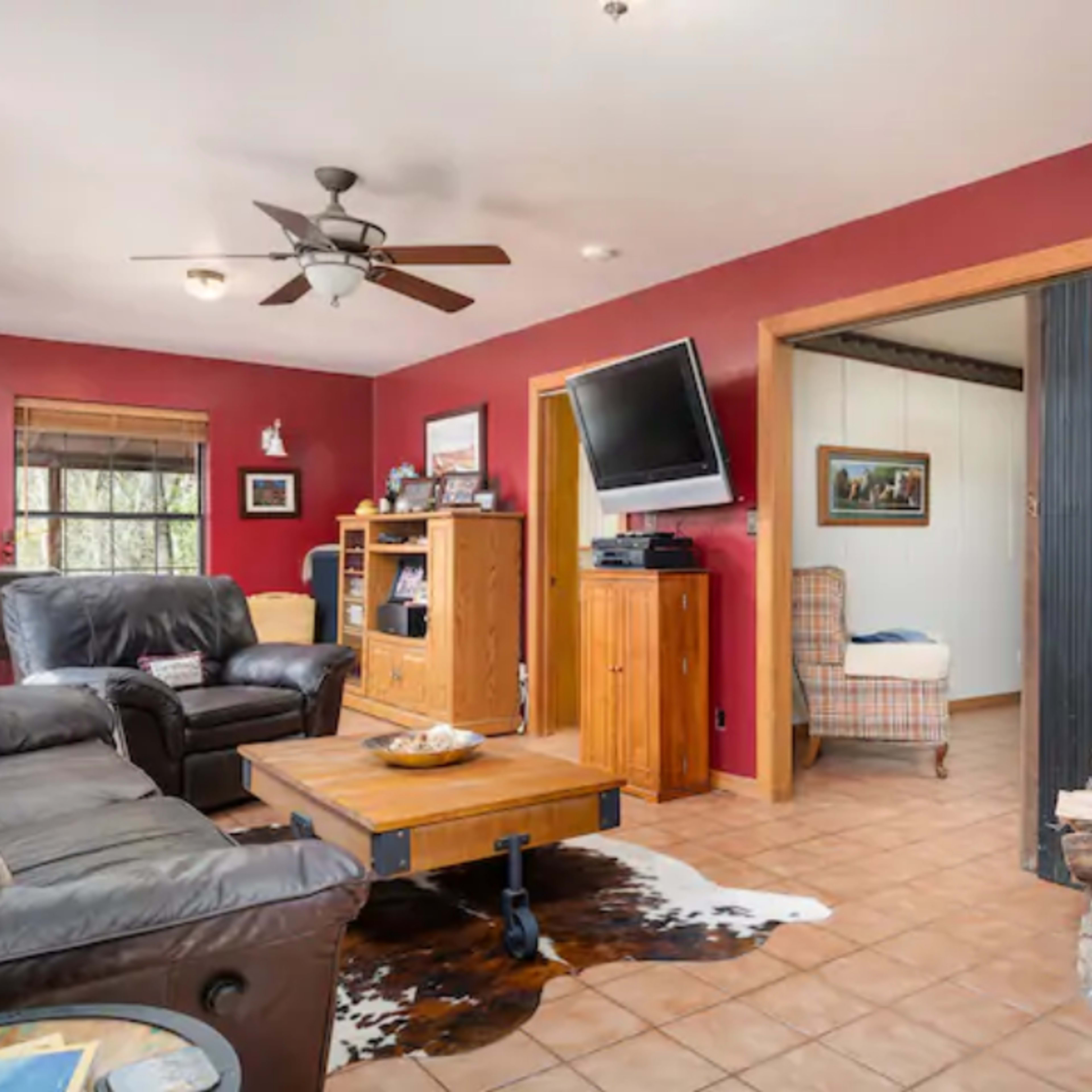 The living room features leather sofas, a wooden coffee table on a tiled floor, a stone fireplace, and a wall-mounted television.