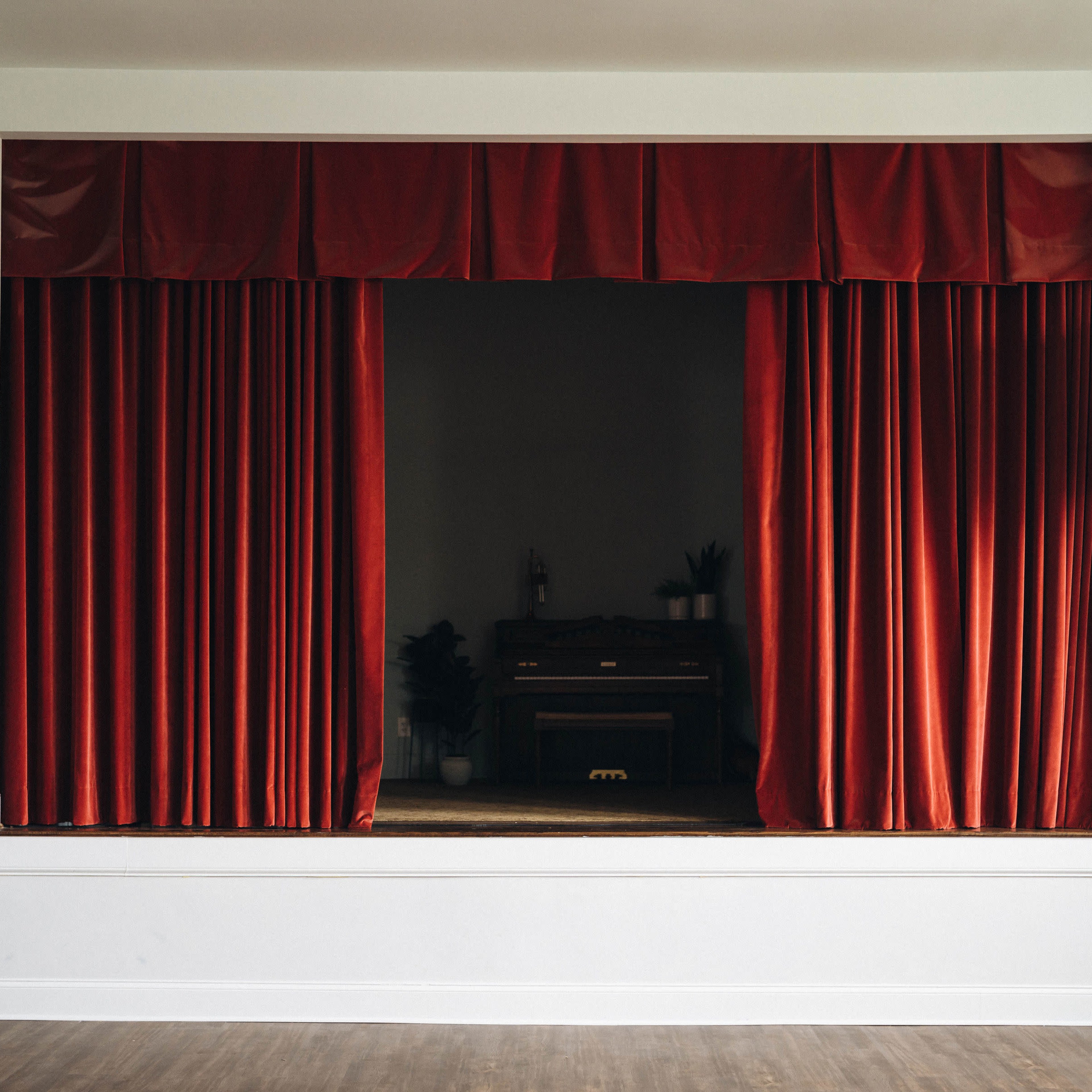 A stage with red curtains and a wooden piano set against a neutral background.