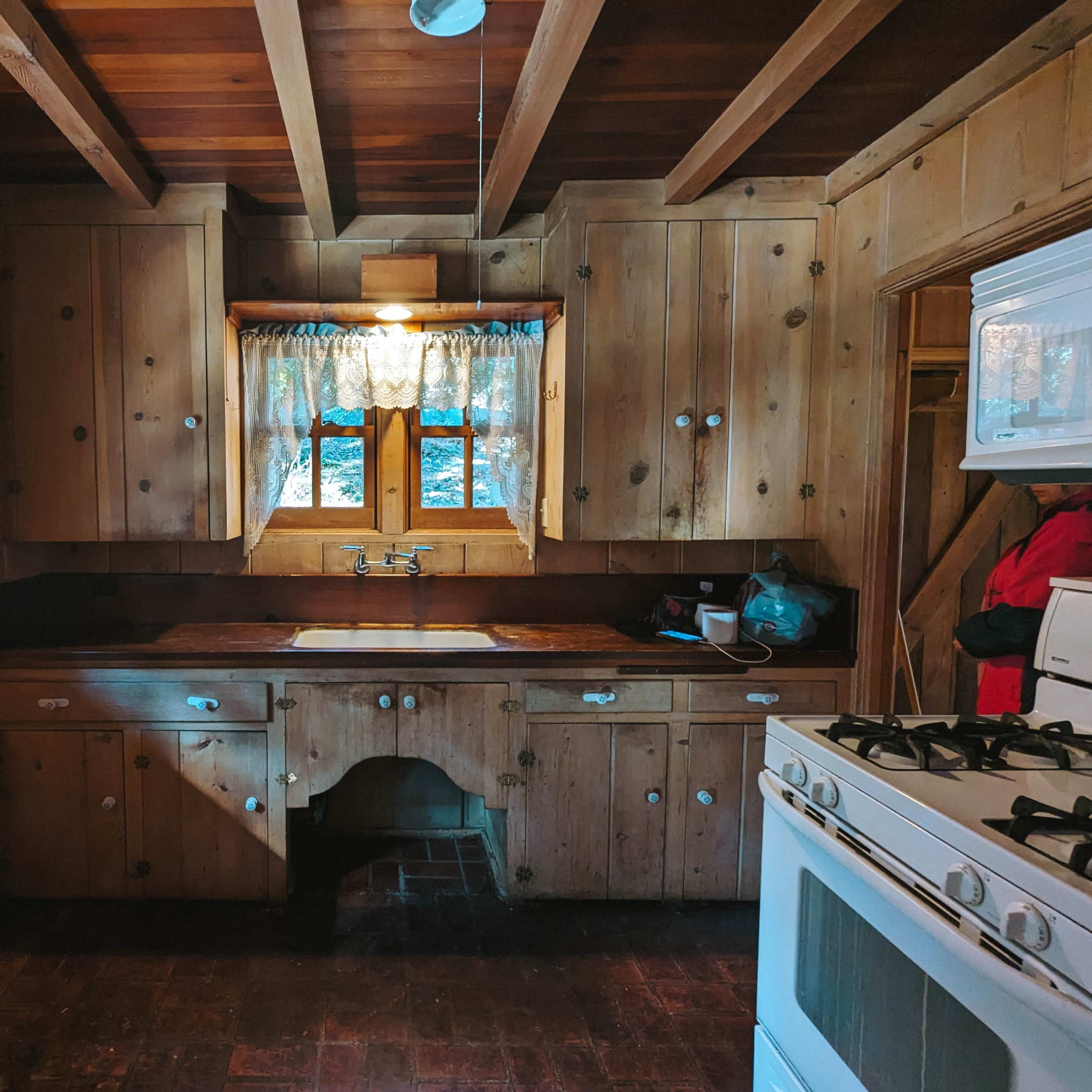 A rustic kitchen with wooden walls, a sink against the back wall, and a white stove.