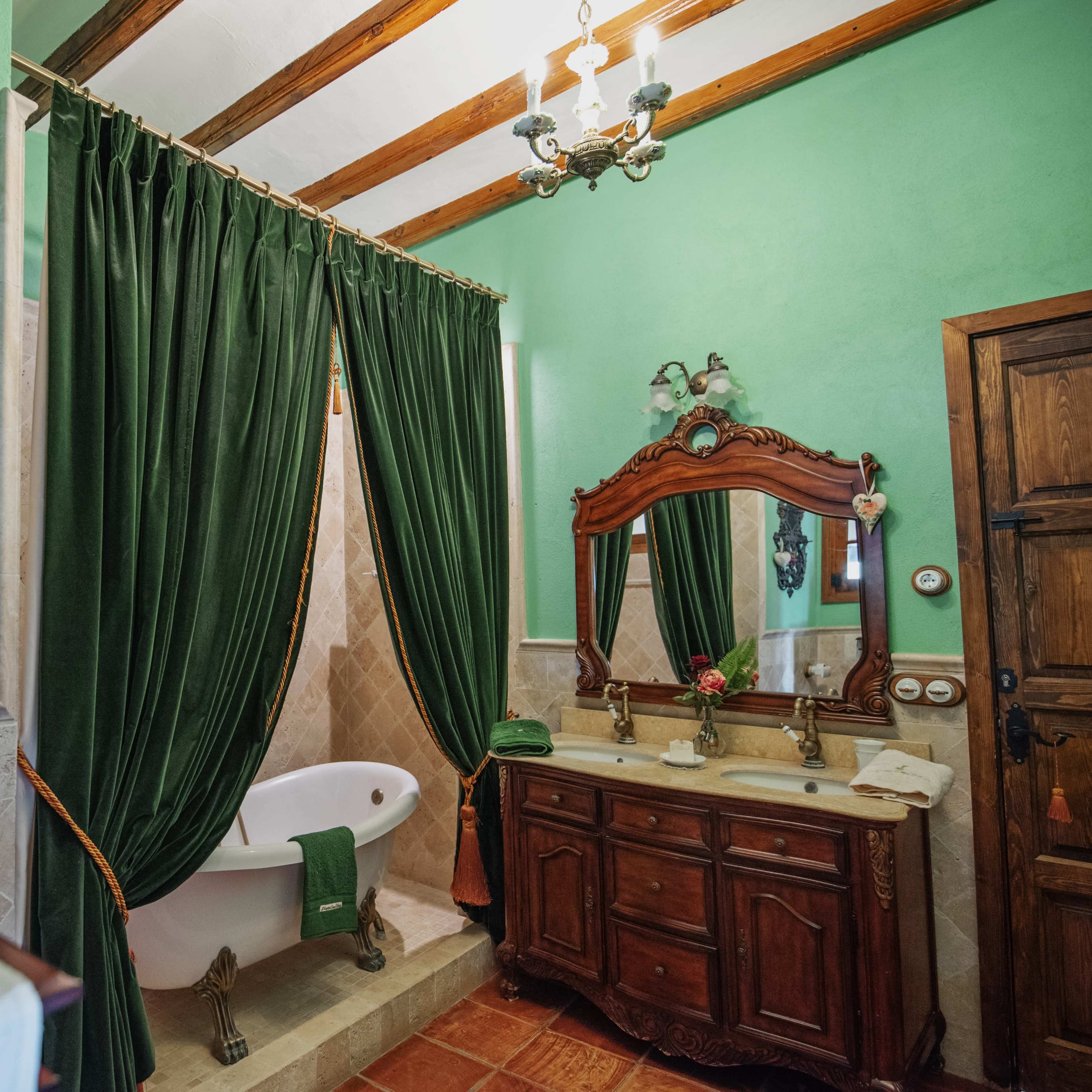 A bathroom features a freestanding bathtub, wooden cabinetry with a sink, and green curtains, all set against a light green wall and wooden beams.
