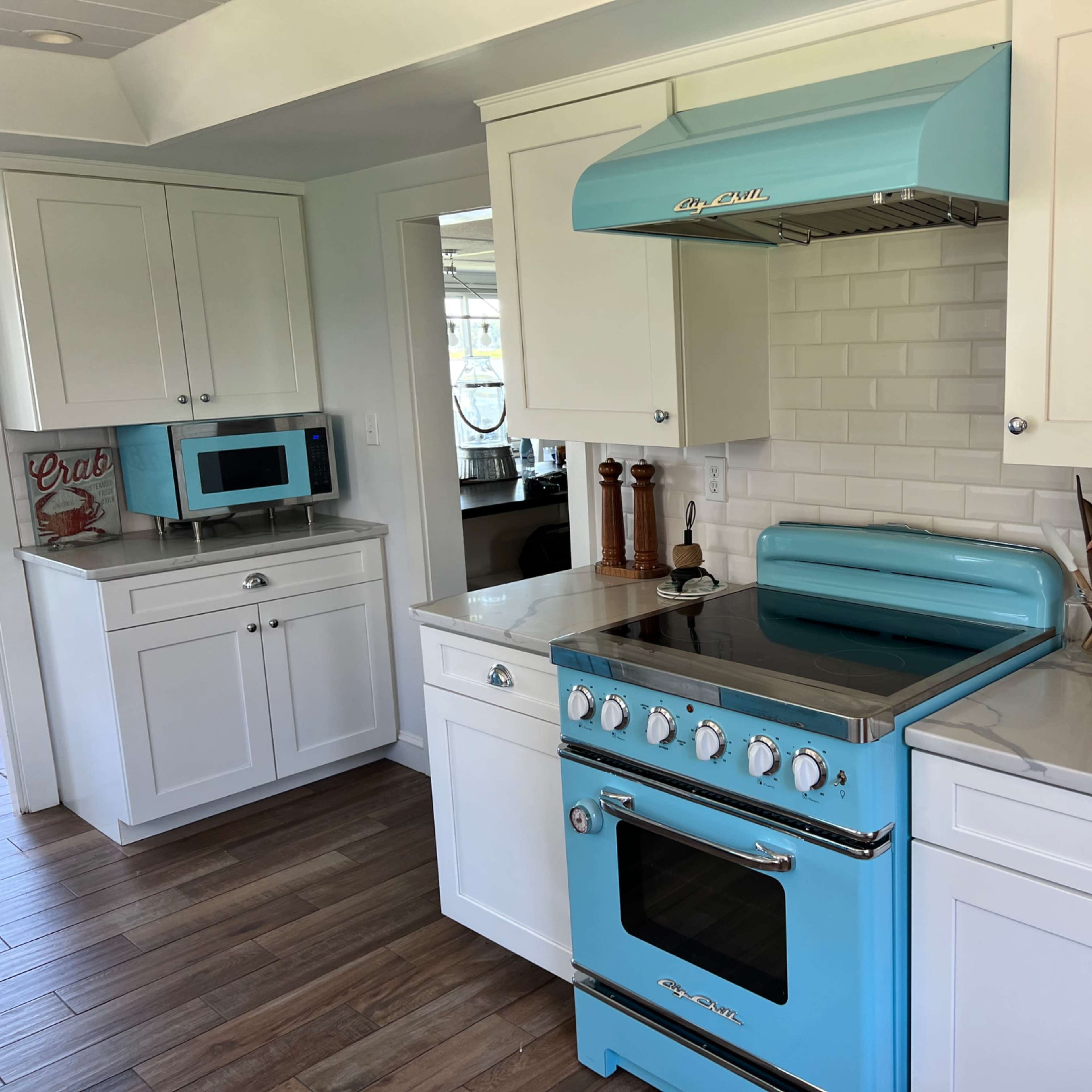 A modern kitchen featuring a light blue retro-style stove, white cabinetry, and a large window.