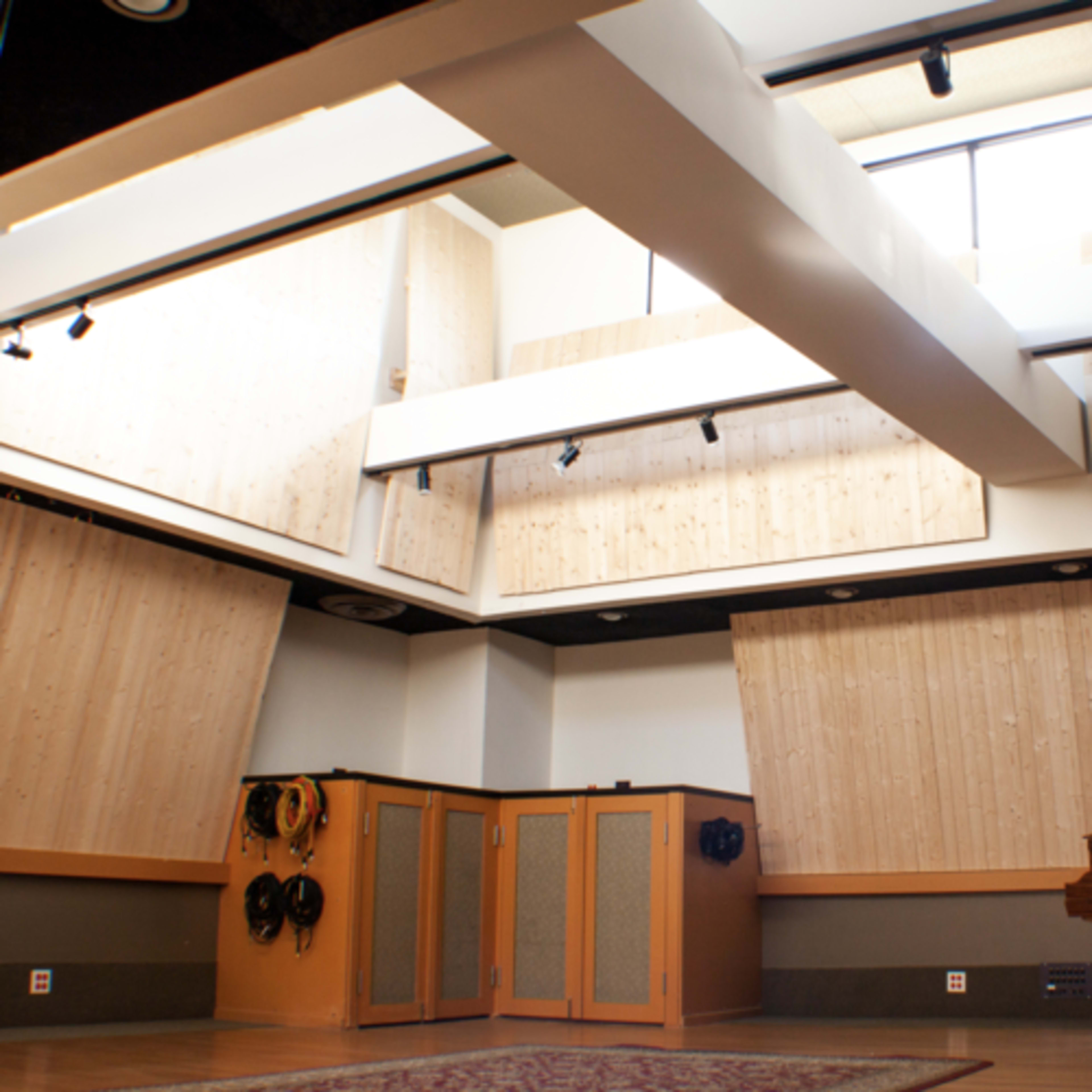 A spacious recording studio with wooden paneling, multiple windows, and a grand piano positioned in the corner.