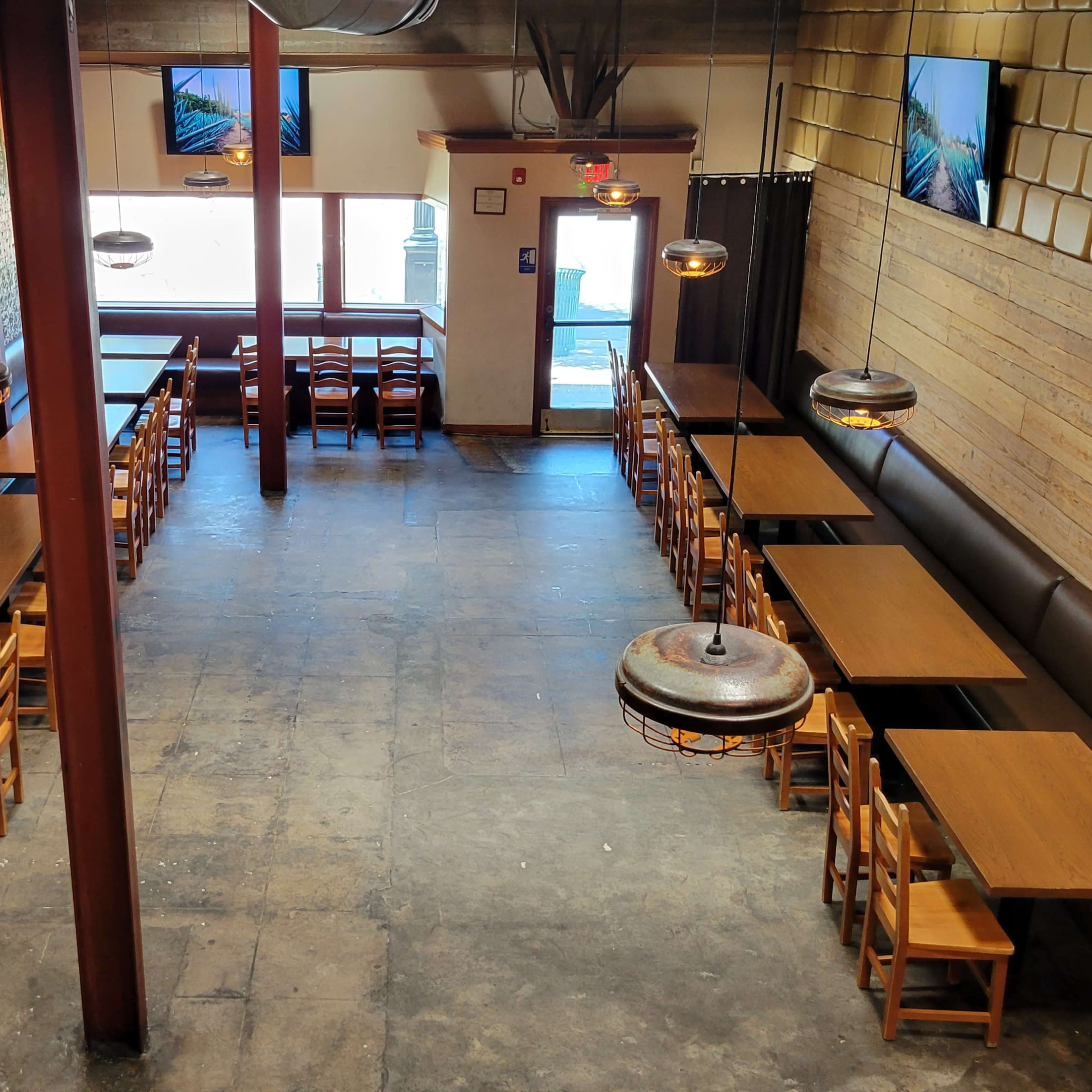 An indoor restaurant setting with wooden tables arranged in rows, brick and wooden walls, and multiple televisions mounted on the walls.