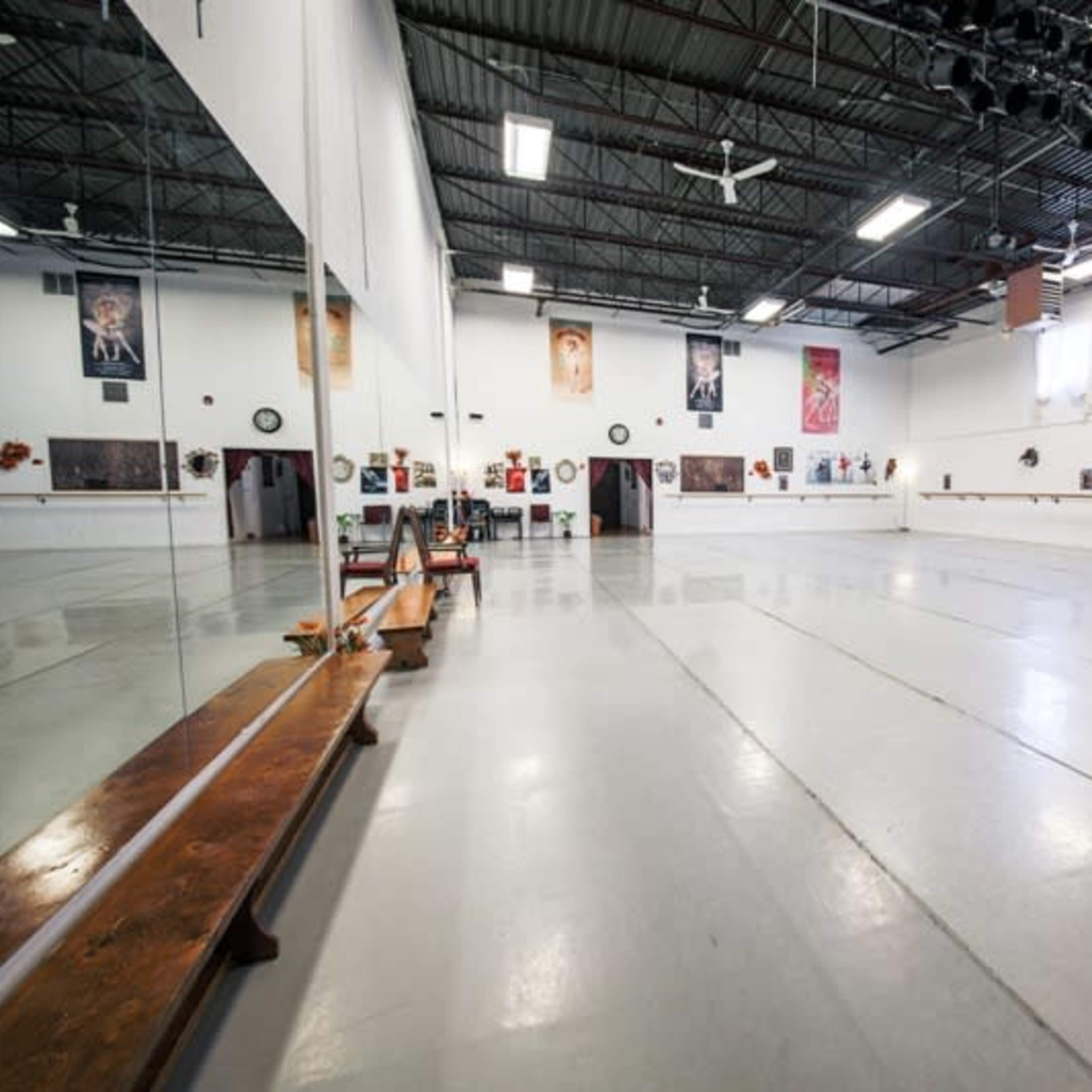 A spacious dance studio with mirrors, a wooden ballet bar, and framed photographs on the walls.