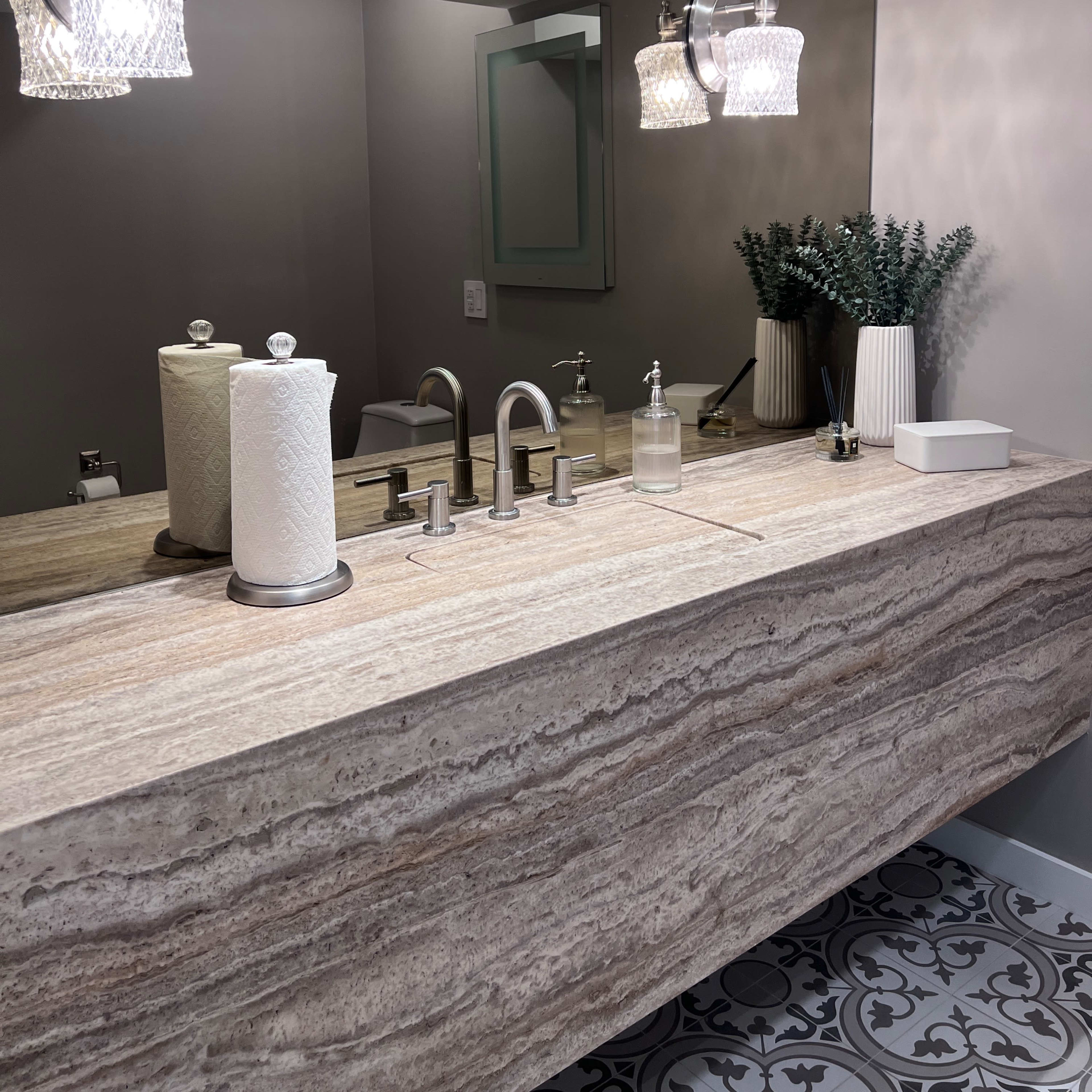A modern bathroom features a polished stone countertop with dual faucets, a large mirror, and stylish light fixtures above.