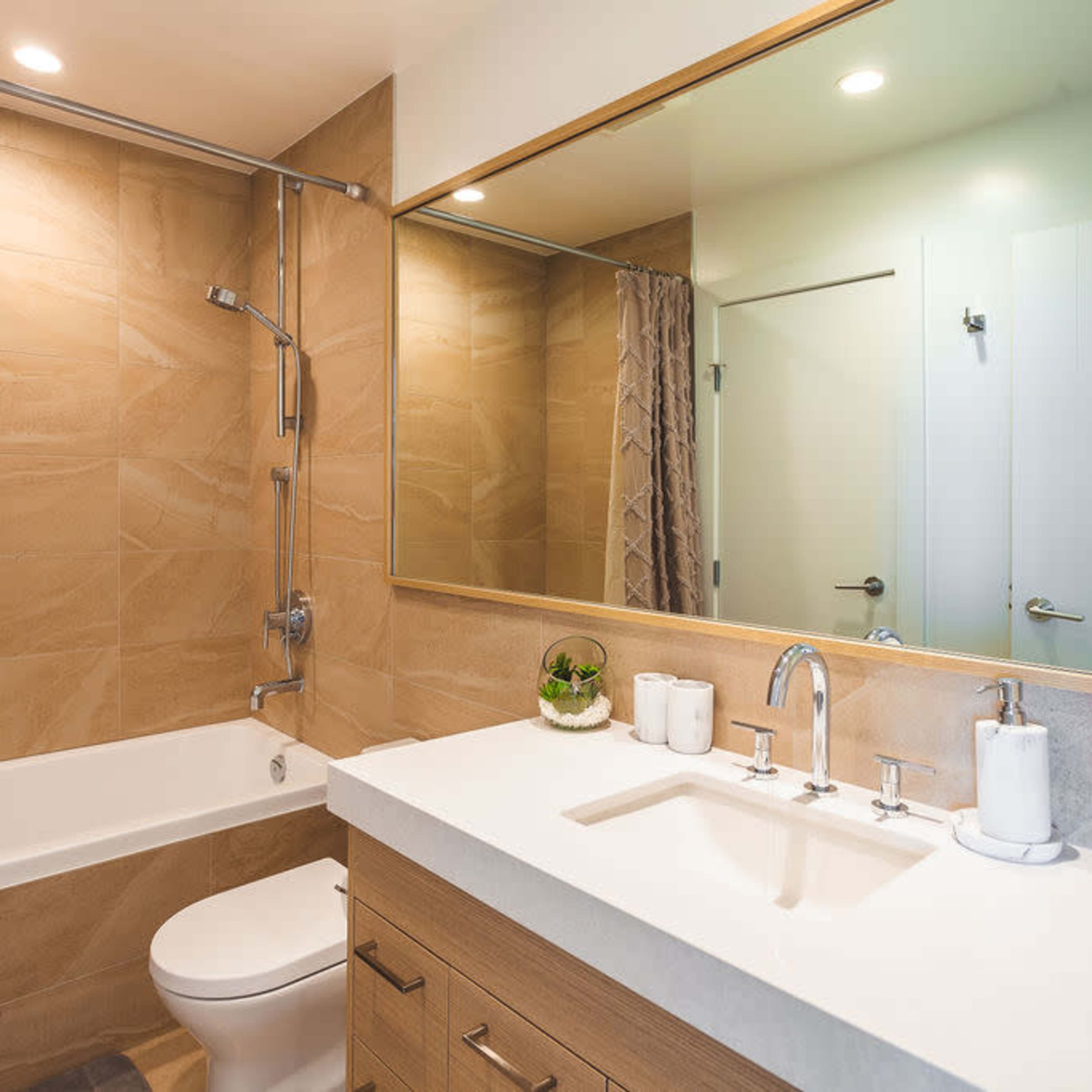 A modern bathroom with a bathtub, shower, toilet, and a double sink vanity beneath a large mirror.