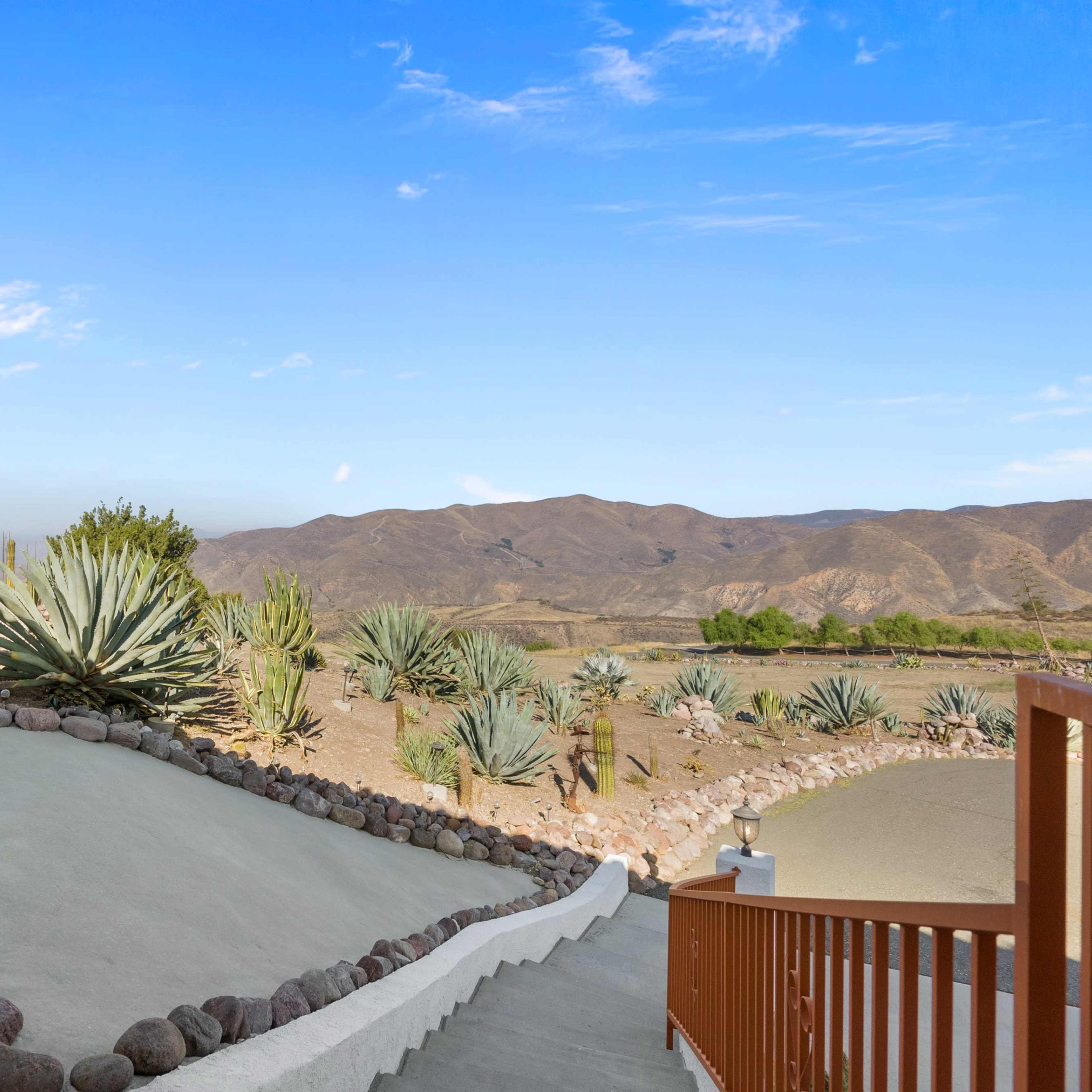 A landscaped outdoor area with stone pathways, agave plants, and a view of rolling hills under a clear sky.