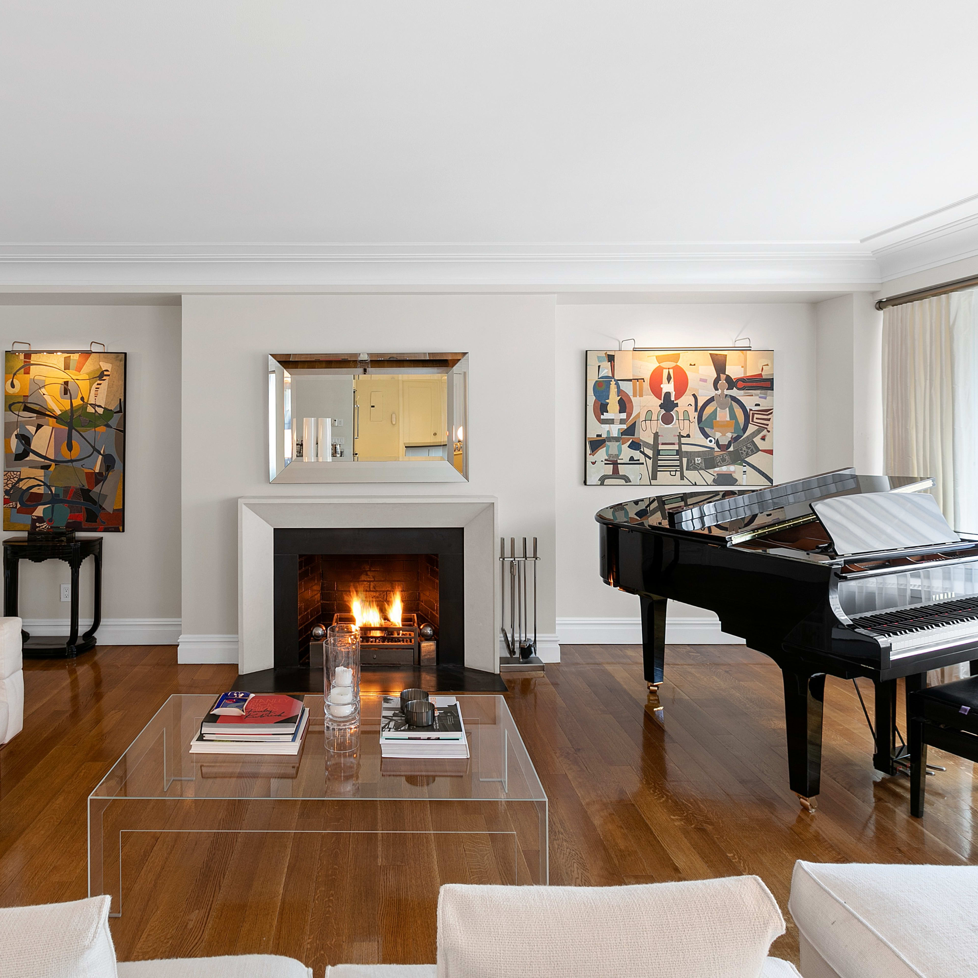 A living room featuring a fireplace, a grand piano, bookshelves, and framed artwork on the walls.