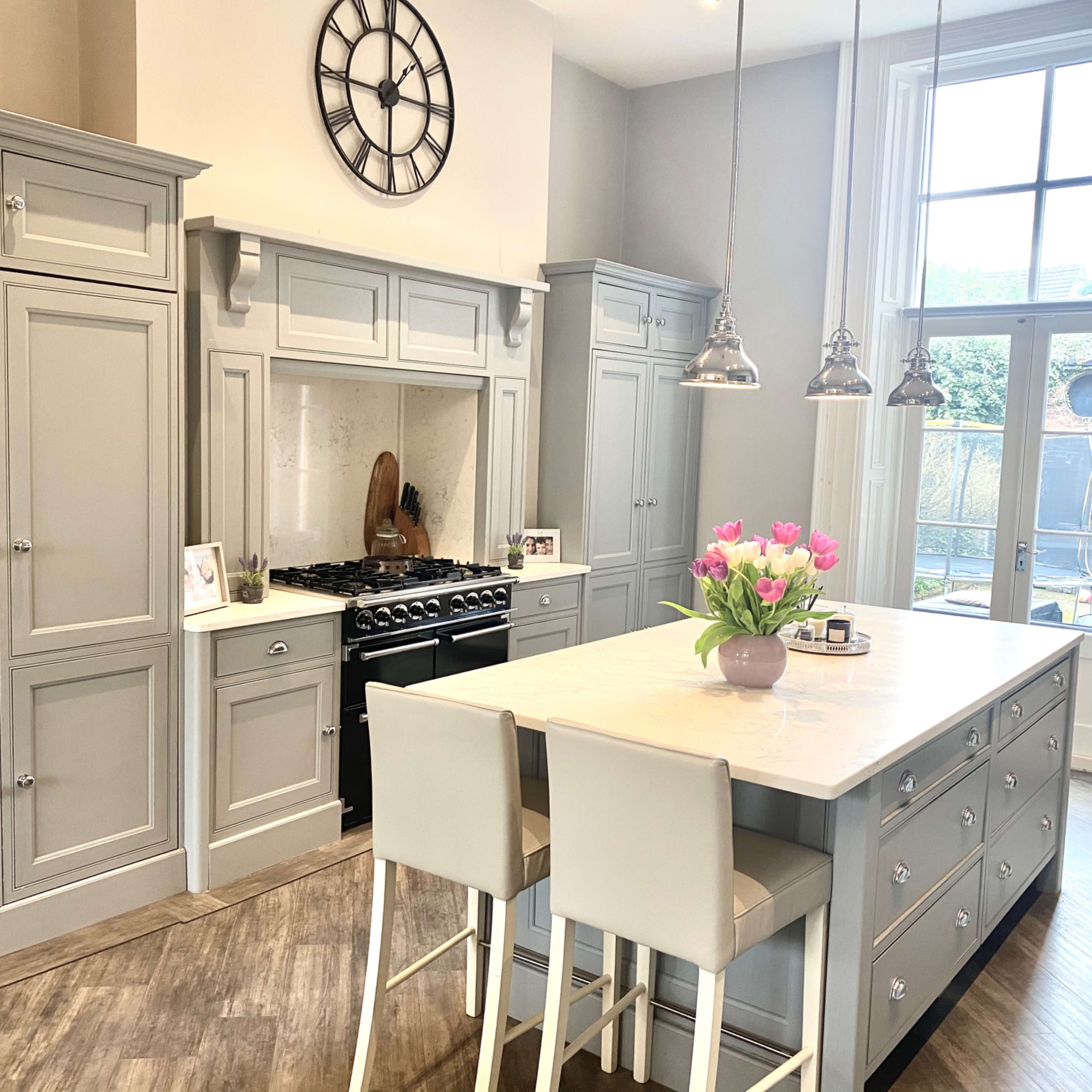 A modern kitchen features gray cabinetry, a gas range, a large island with seating, and a window overlooking an outdoor space.