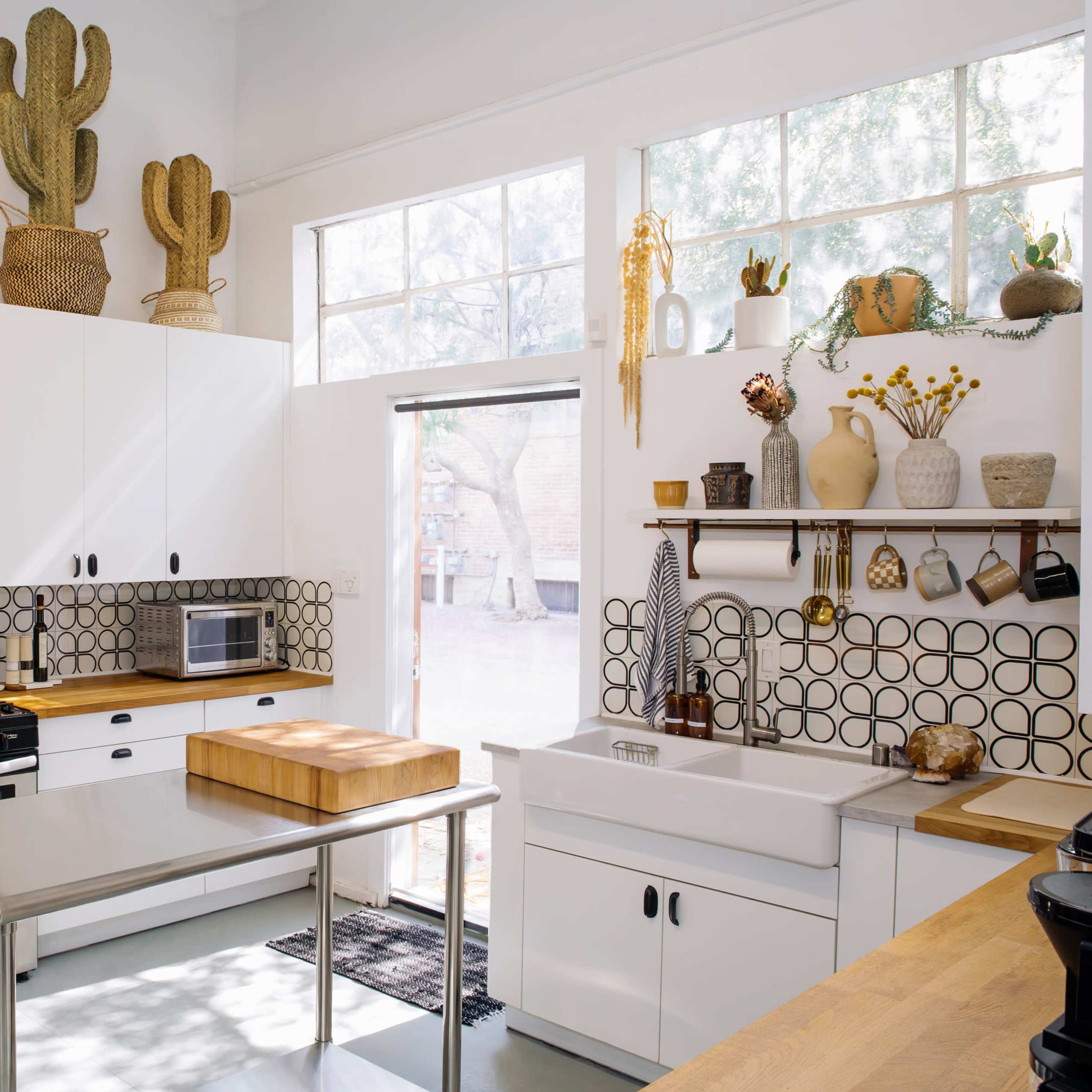 A modern kitchen with white cabinetry, a stainless steel refrigerator, a gas stove, and decorative cacti displayed above the cabinets.