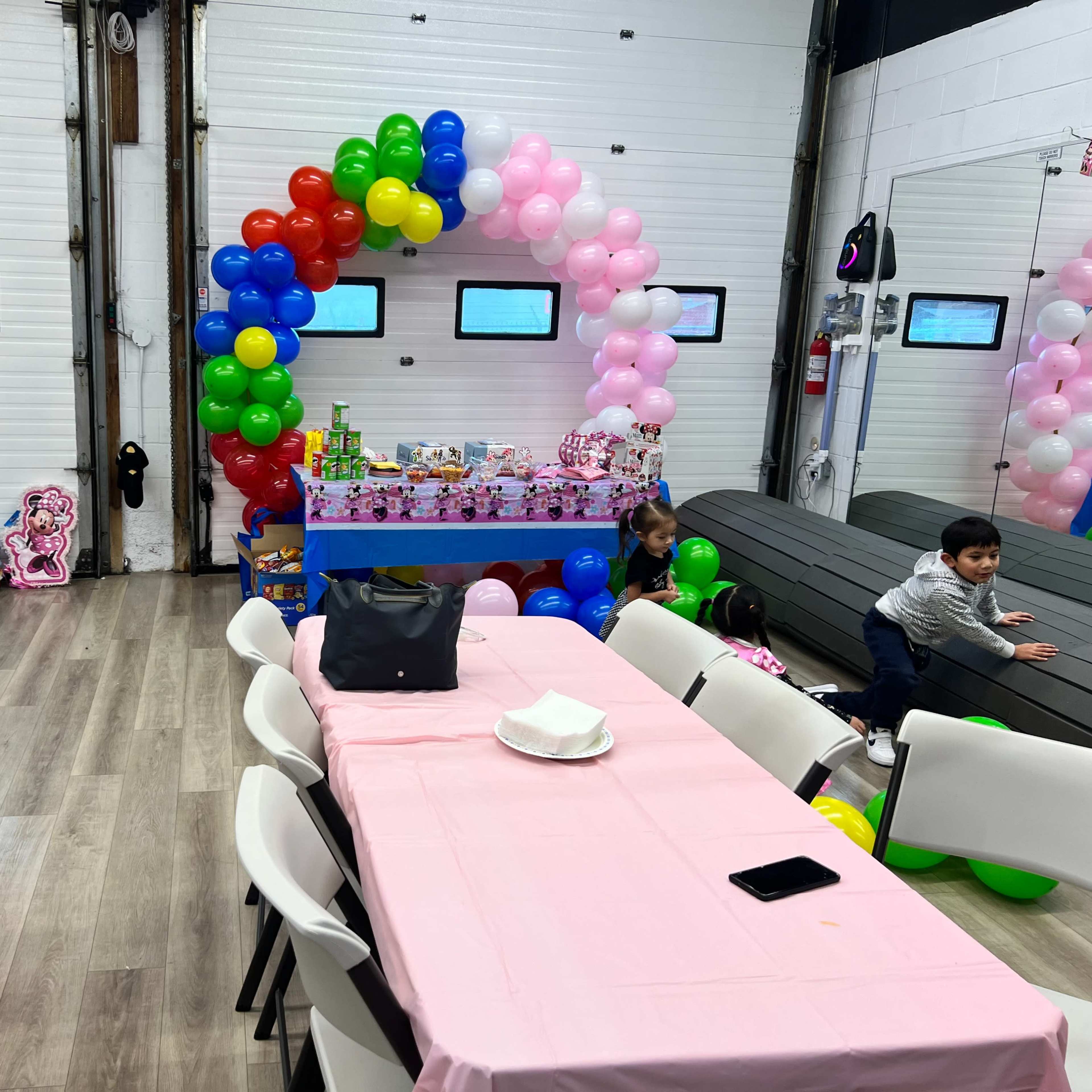 A decorated party venue featuring colorful balloons, a cake table with gifts, and children playing near the tables.