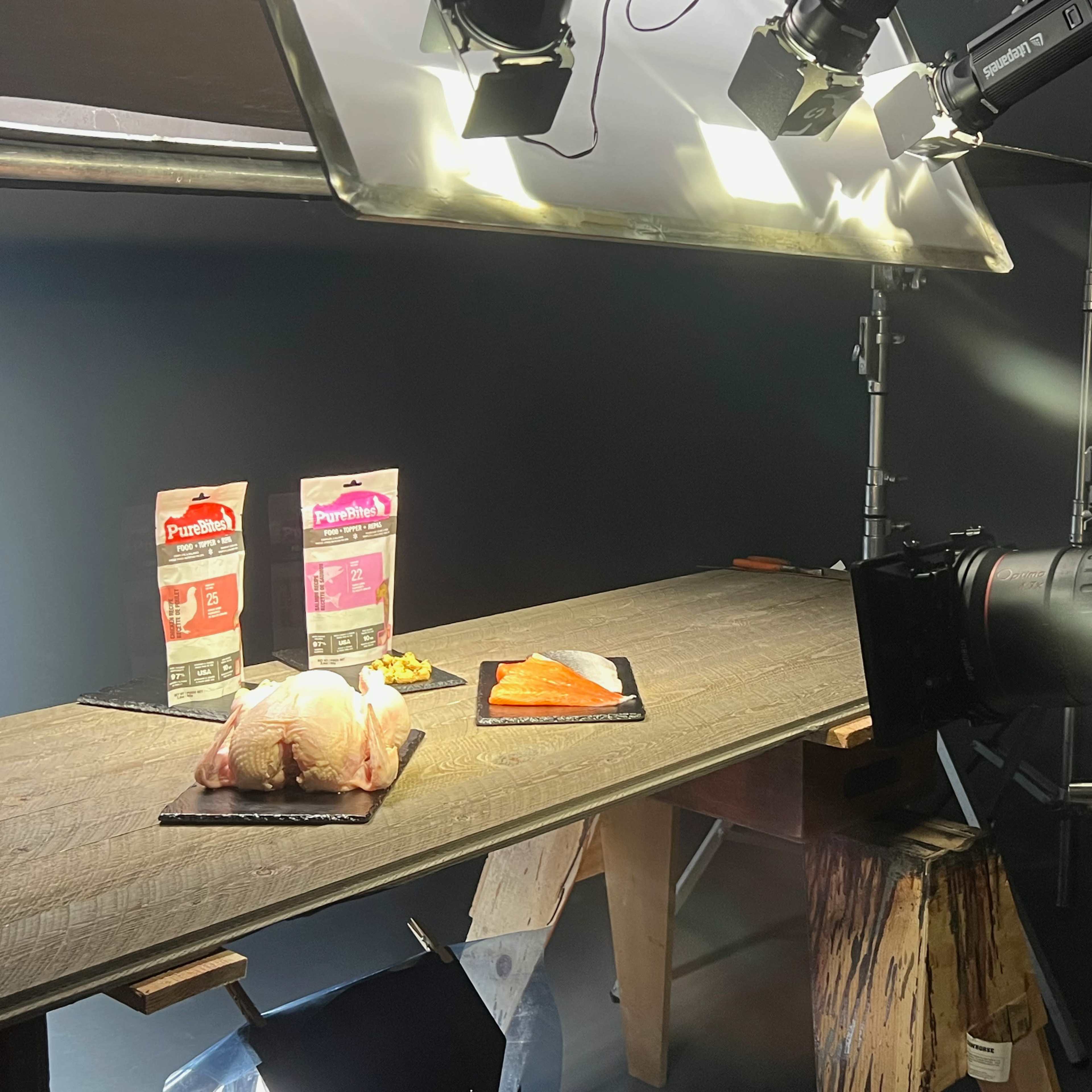 A camera records a scene featuring packaged meat and fish on a wooden table, illuminated by overhead lights.