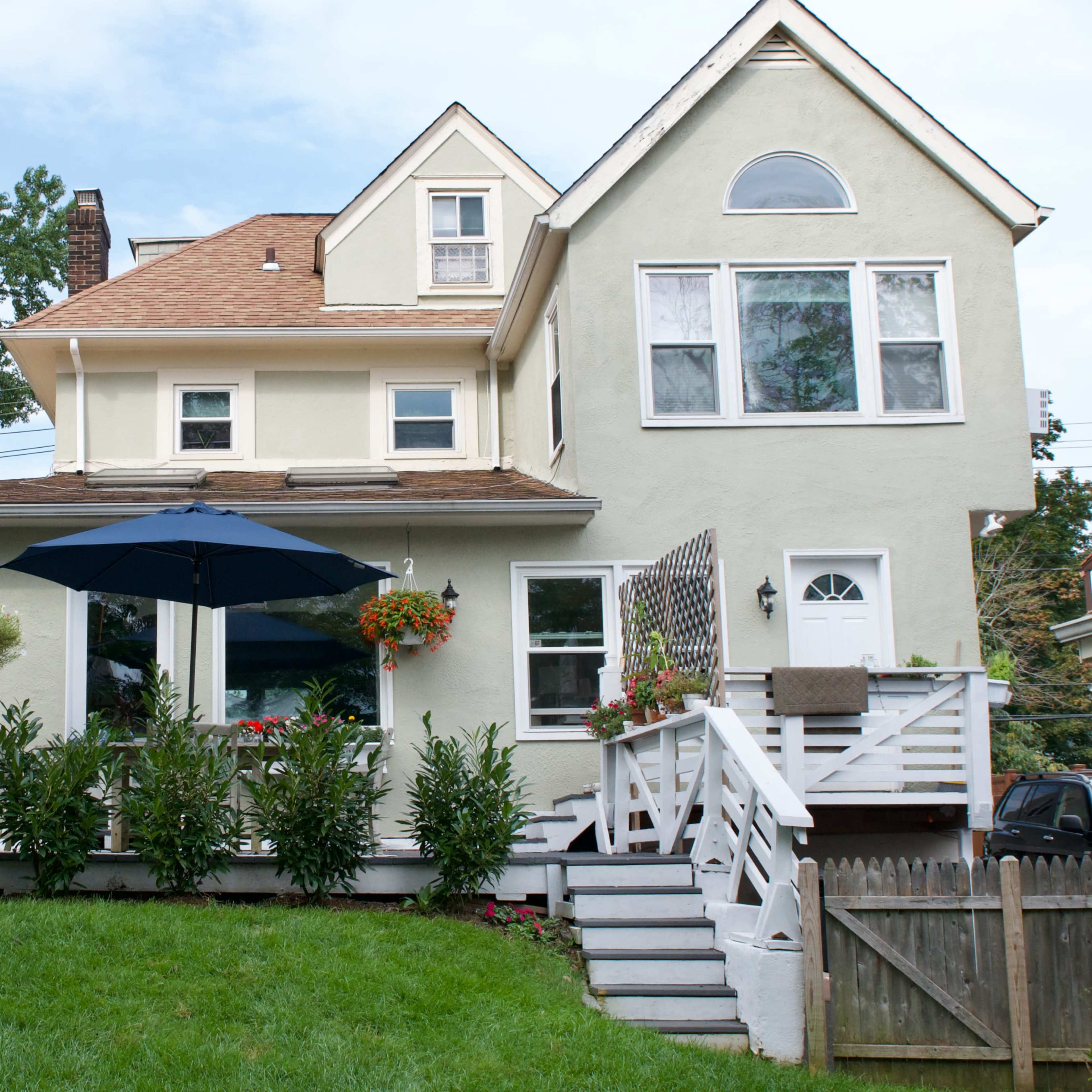 A two-story house with a deck, surrounded by greenery and featuring an umbrella over a seating area.
