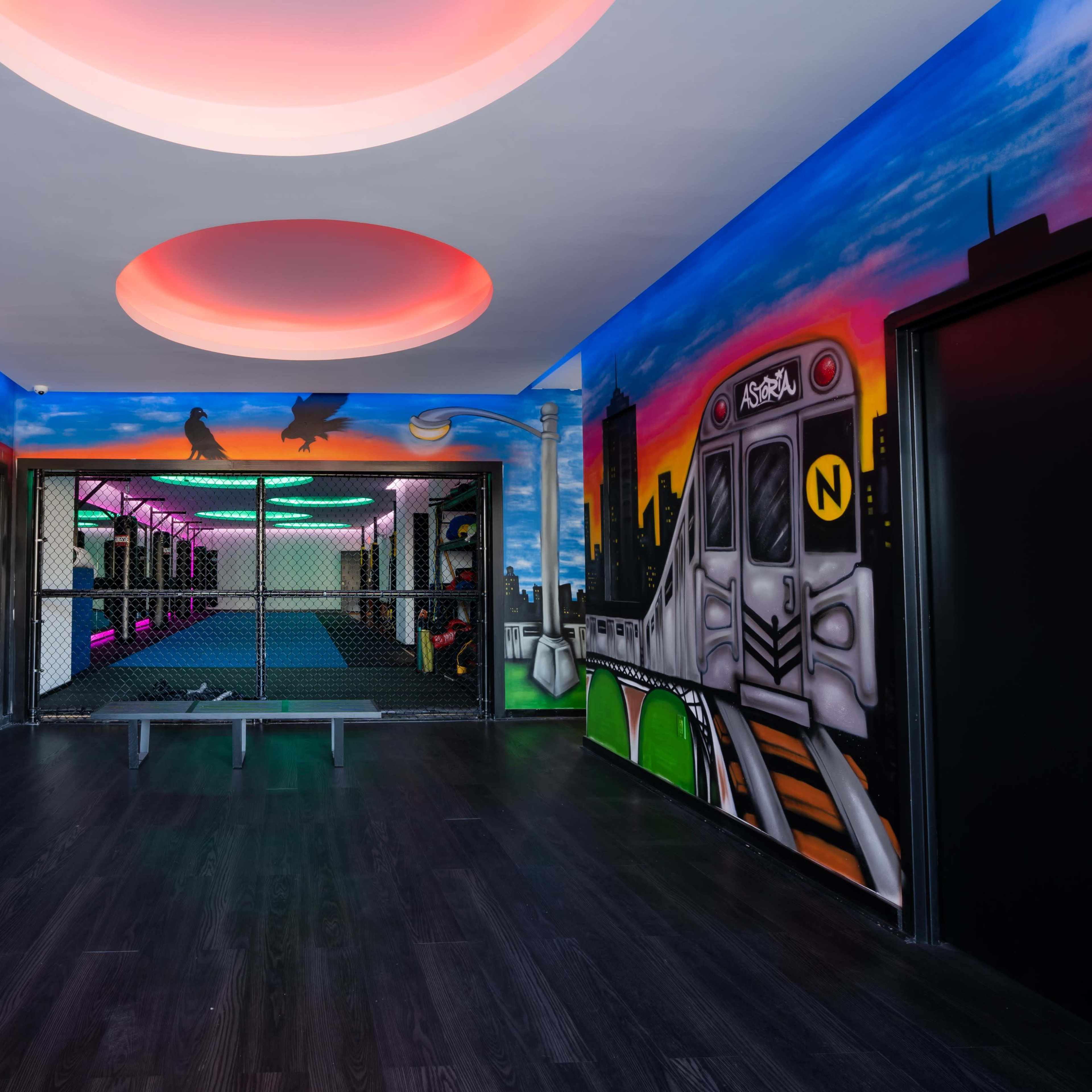 A brightly painted indoor space with colorful murals, featuring a fenced-off area and an arcade game machine in one corner.