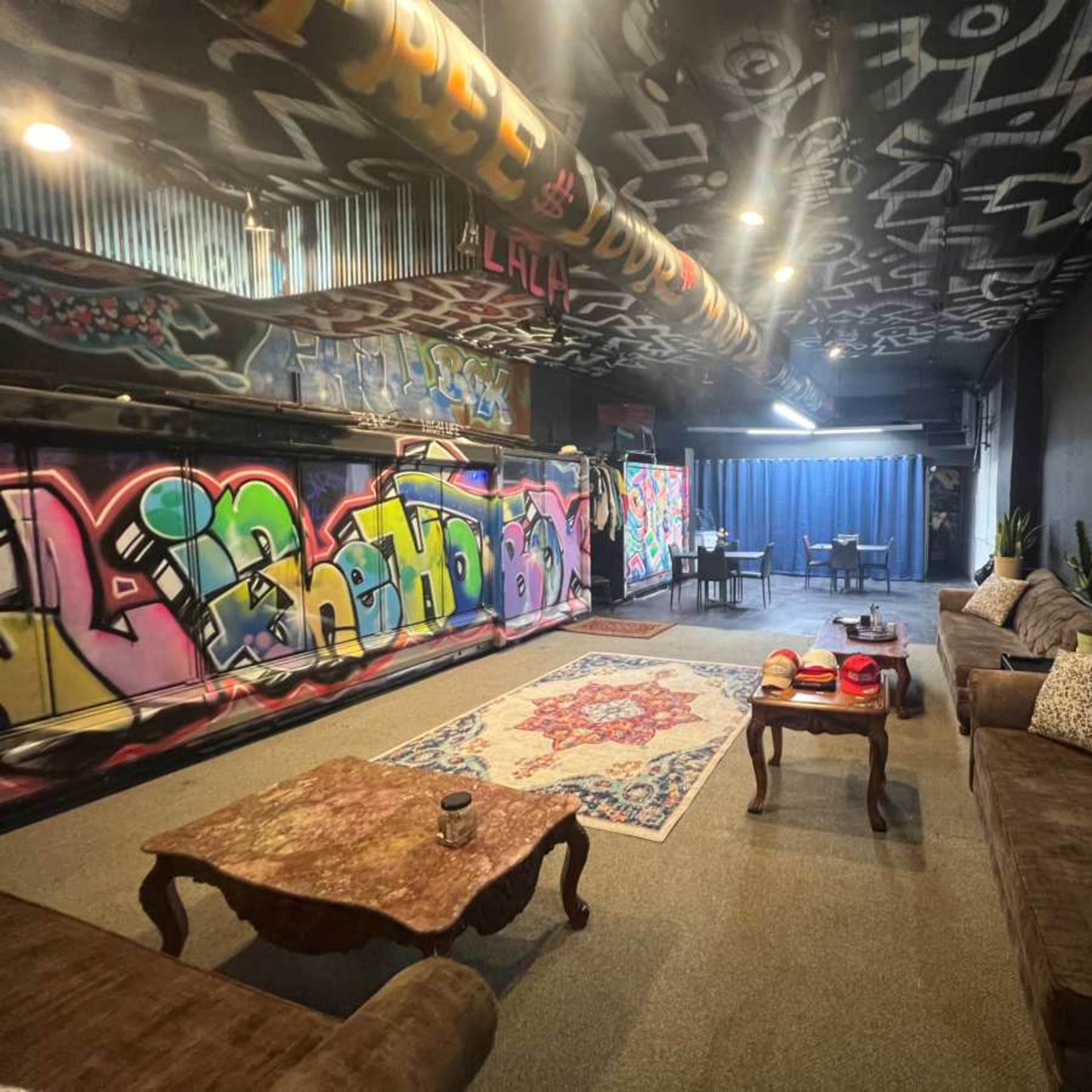A spacious room with graffiti-covered walls, a patterned rug in the center, and seating arranged around a low table.