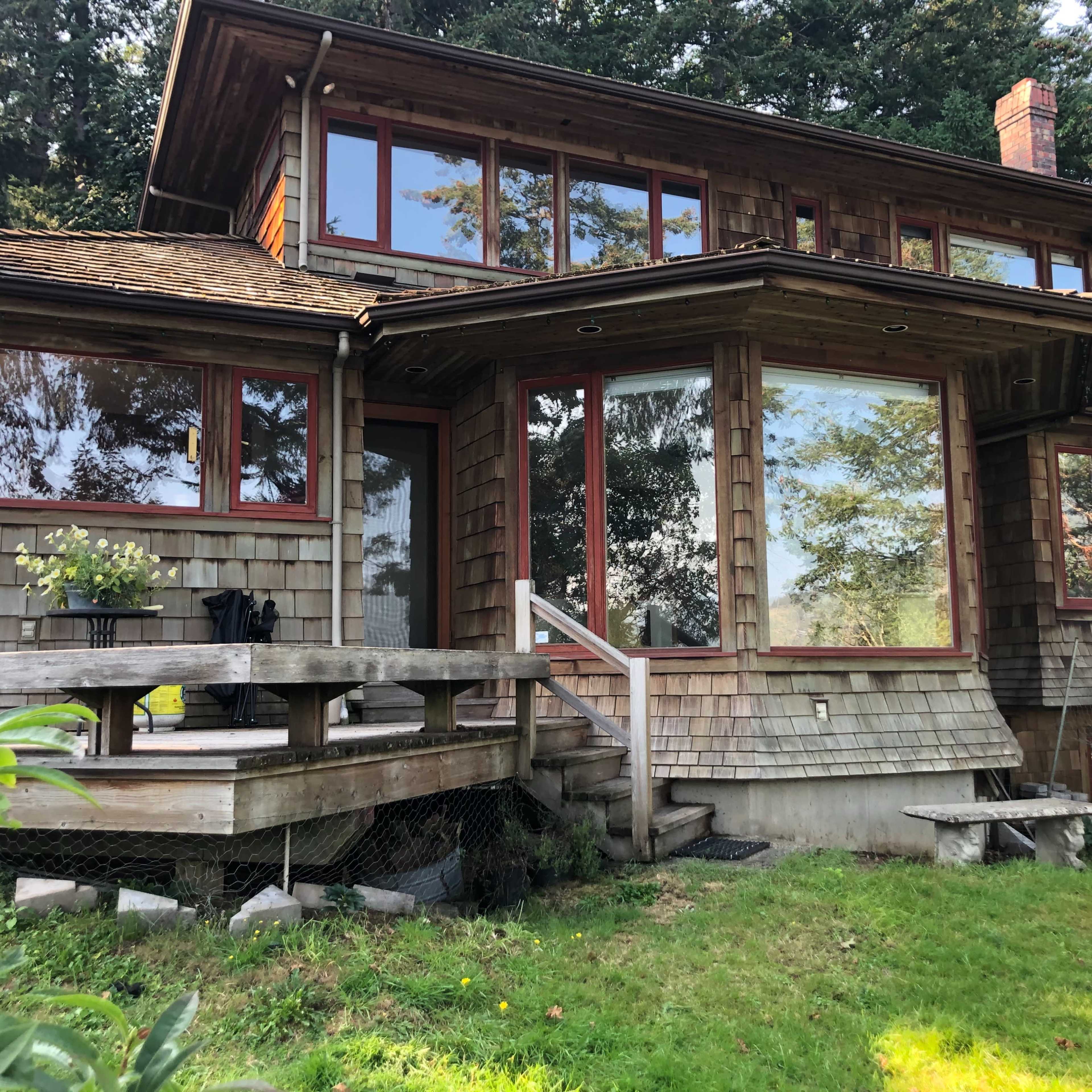 A large wooden house features multiple windows and a deck with stairs leading to the yard.