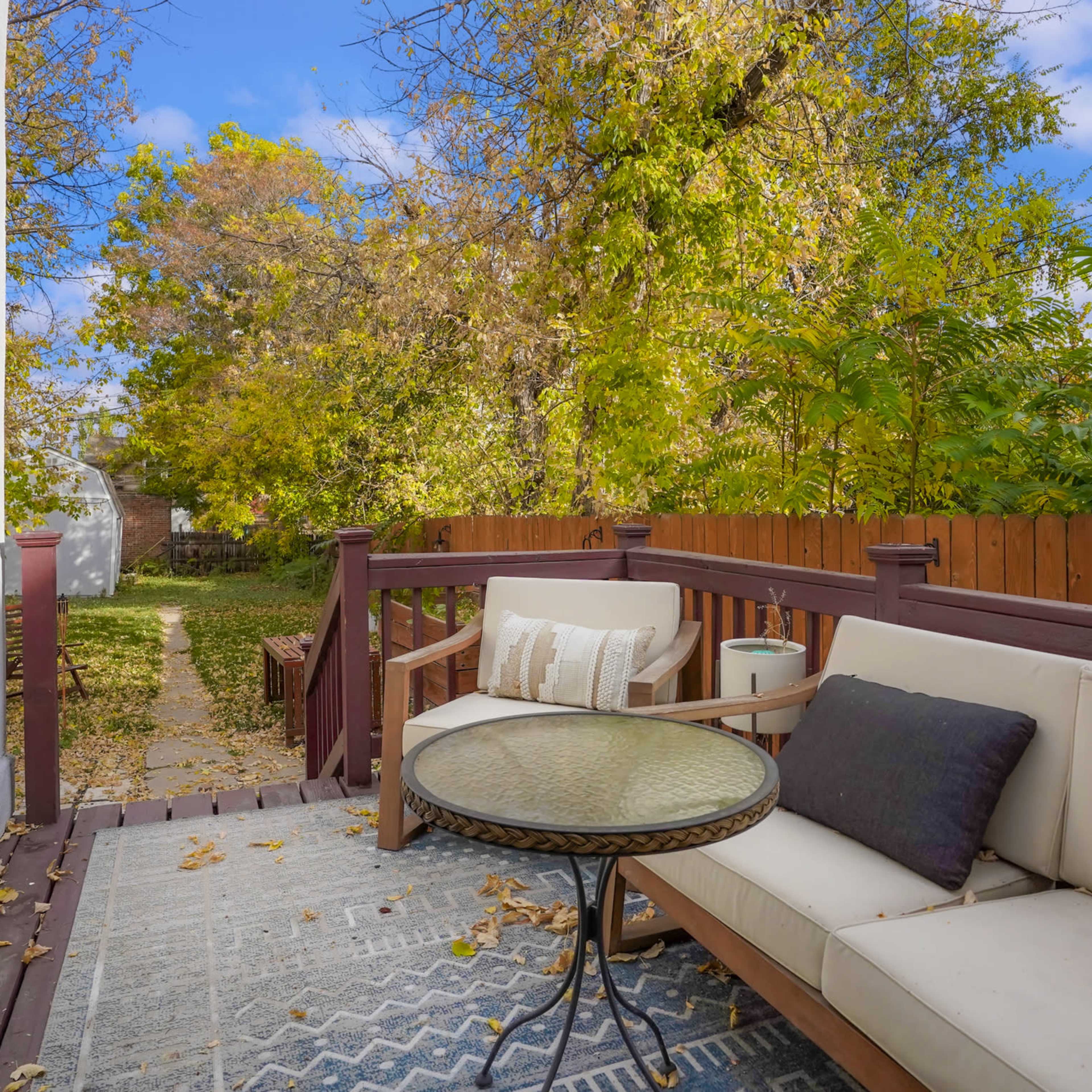 A backyard deck with a seating area and a pathway leading to a garden area surrounded by trees.