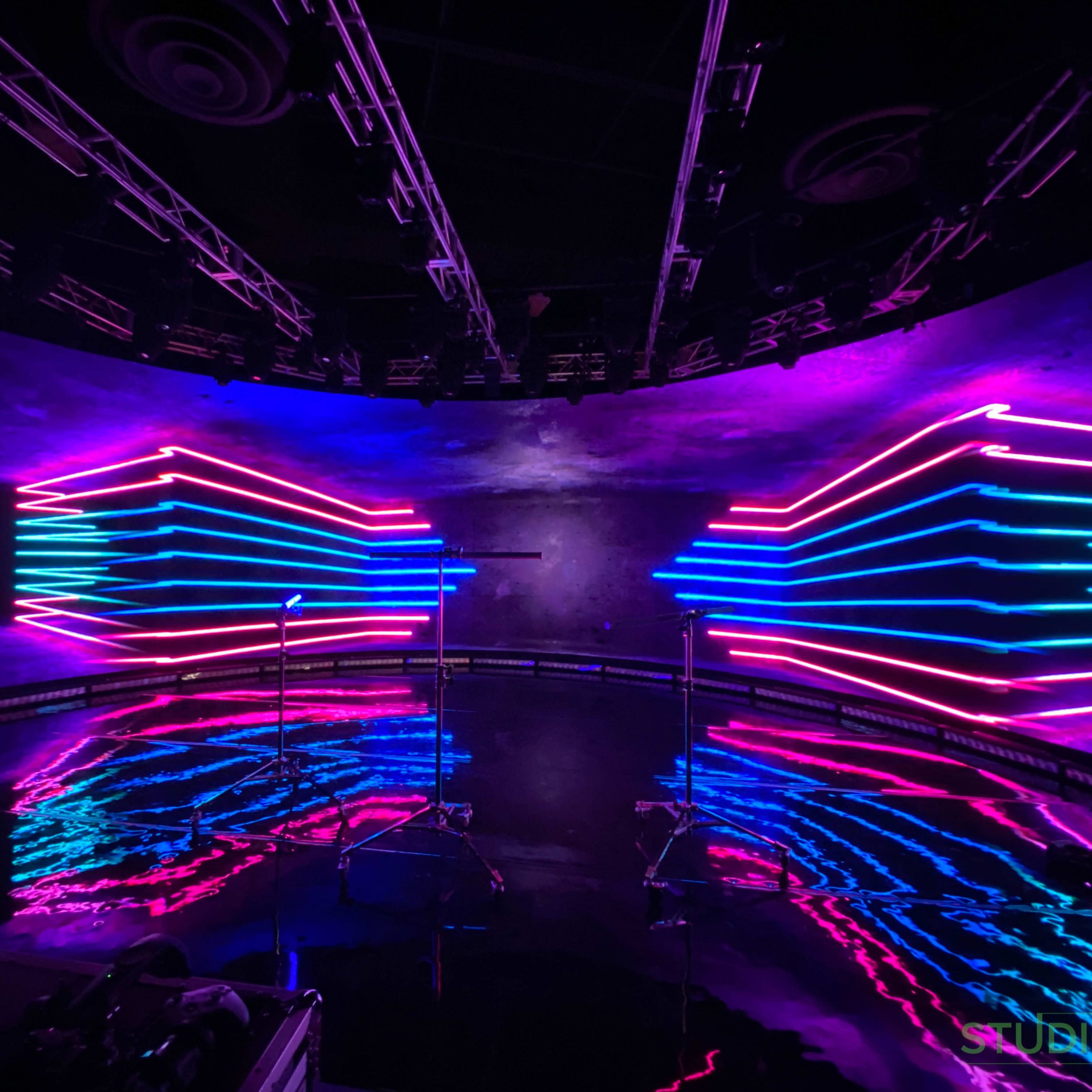 A stage with neon lights arranged in a symmetrical pattern, reflecting off a glossy floor.