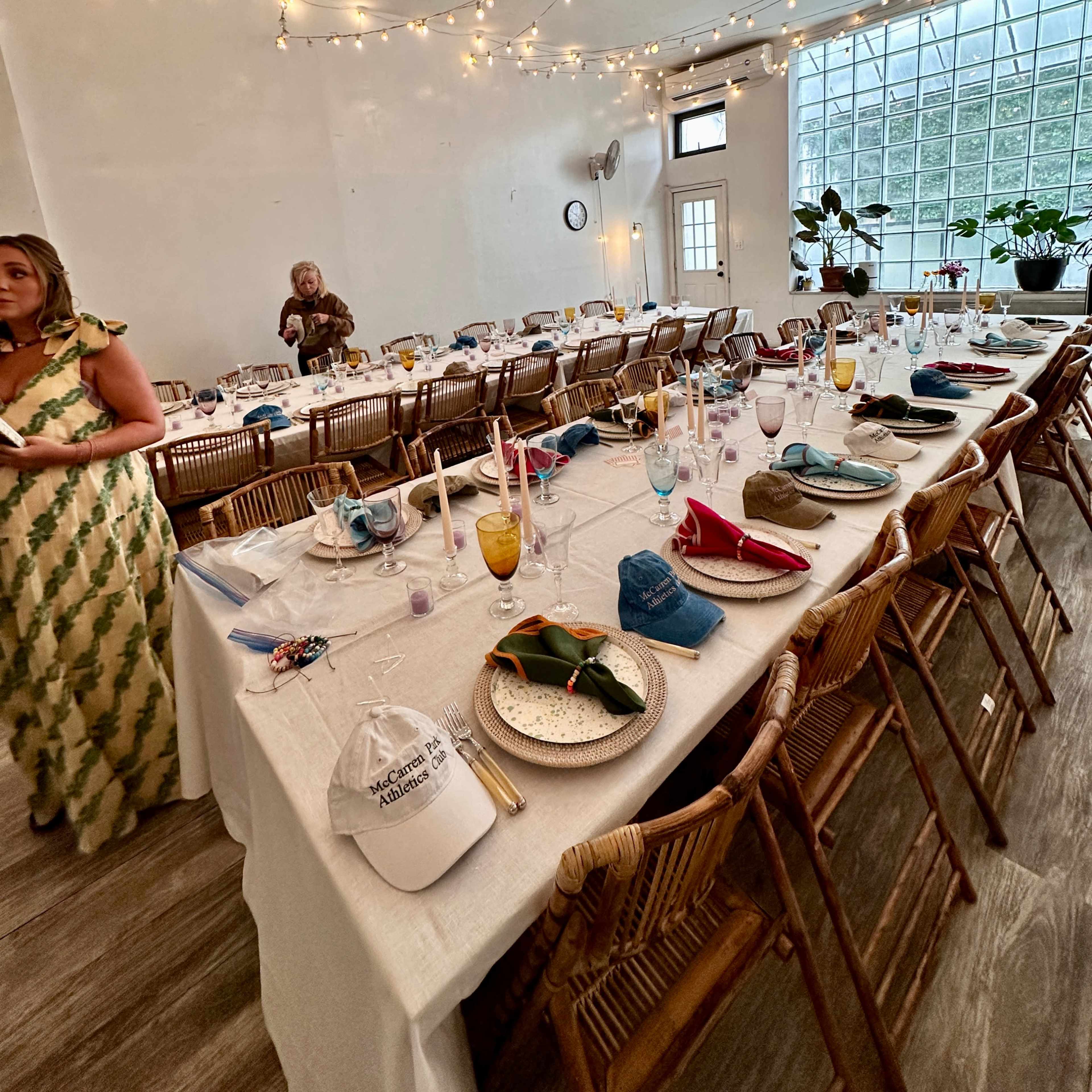 The scene features a large dining table set with elegant place settings and decorated with string lights overhead in a bright, open room.