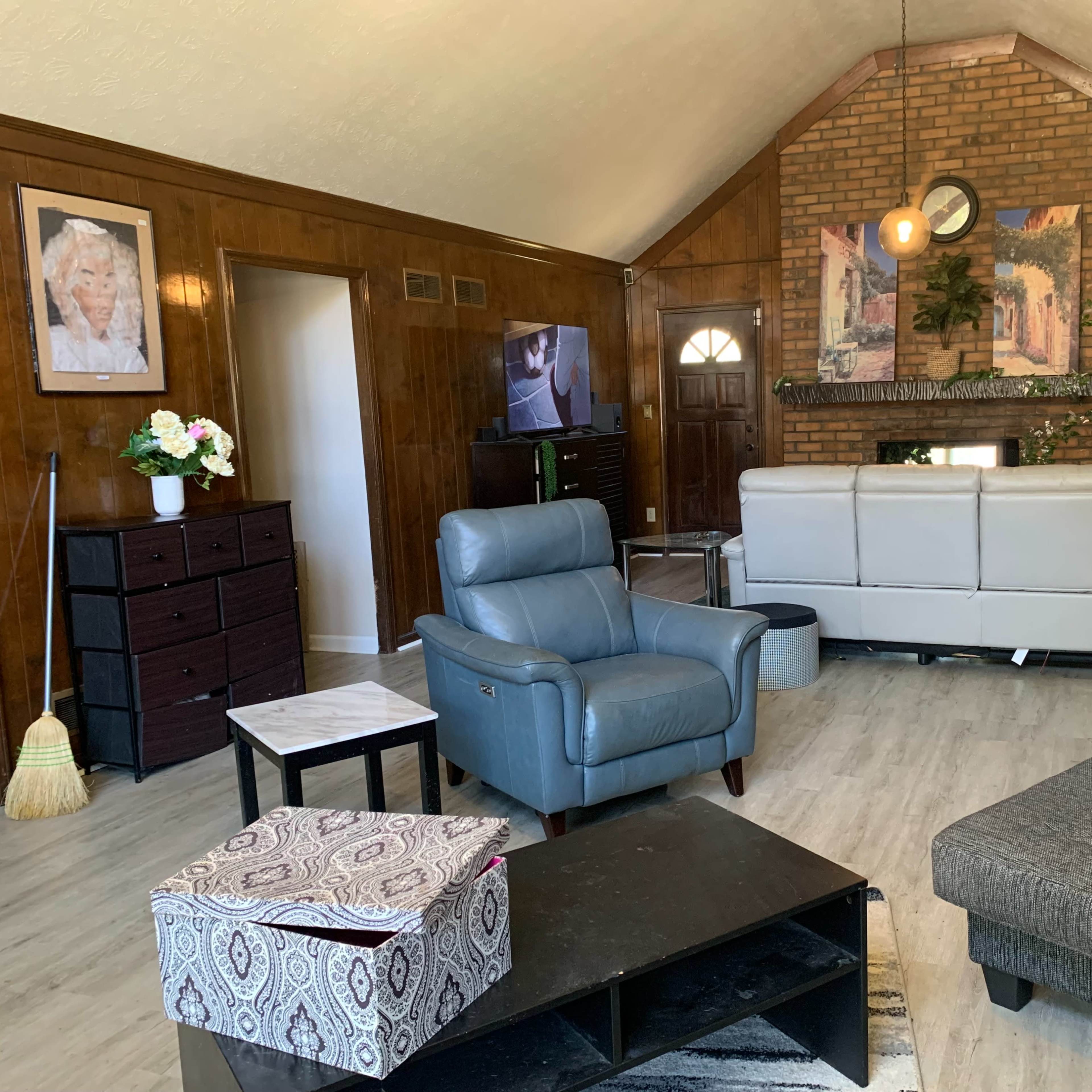 The living room features a mix of seating options, a large wall-mounted television, and wooden paneling, with a brick fireplace as a focal point.