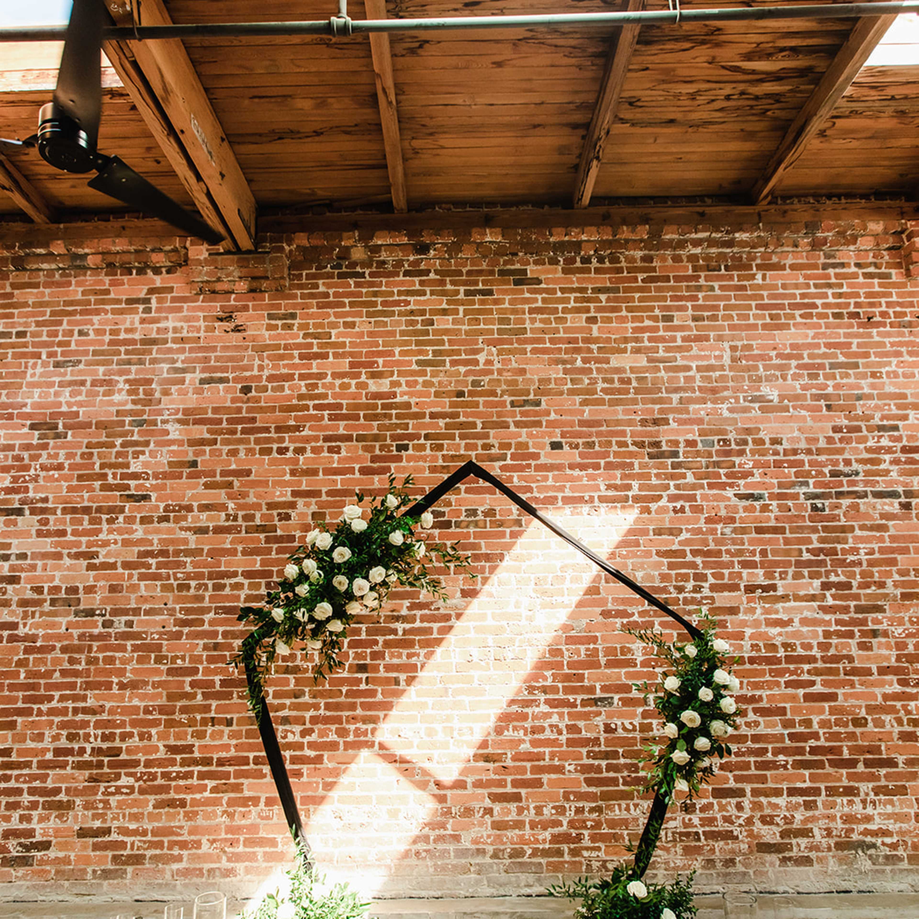 A wedding arch decorated with flowers and ribbons, set against a brick wall with candles placed on the floor.