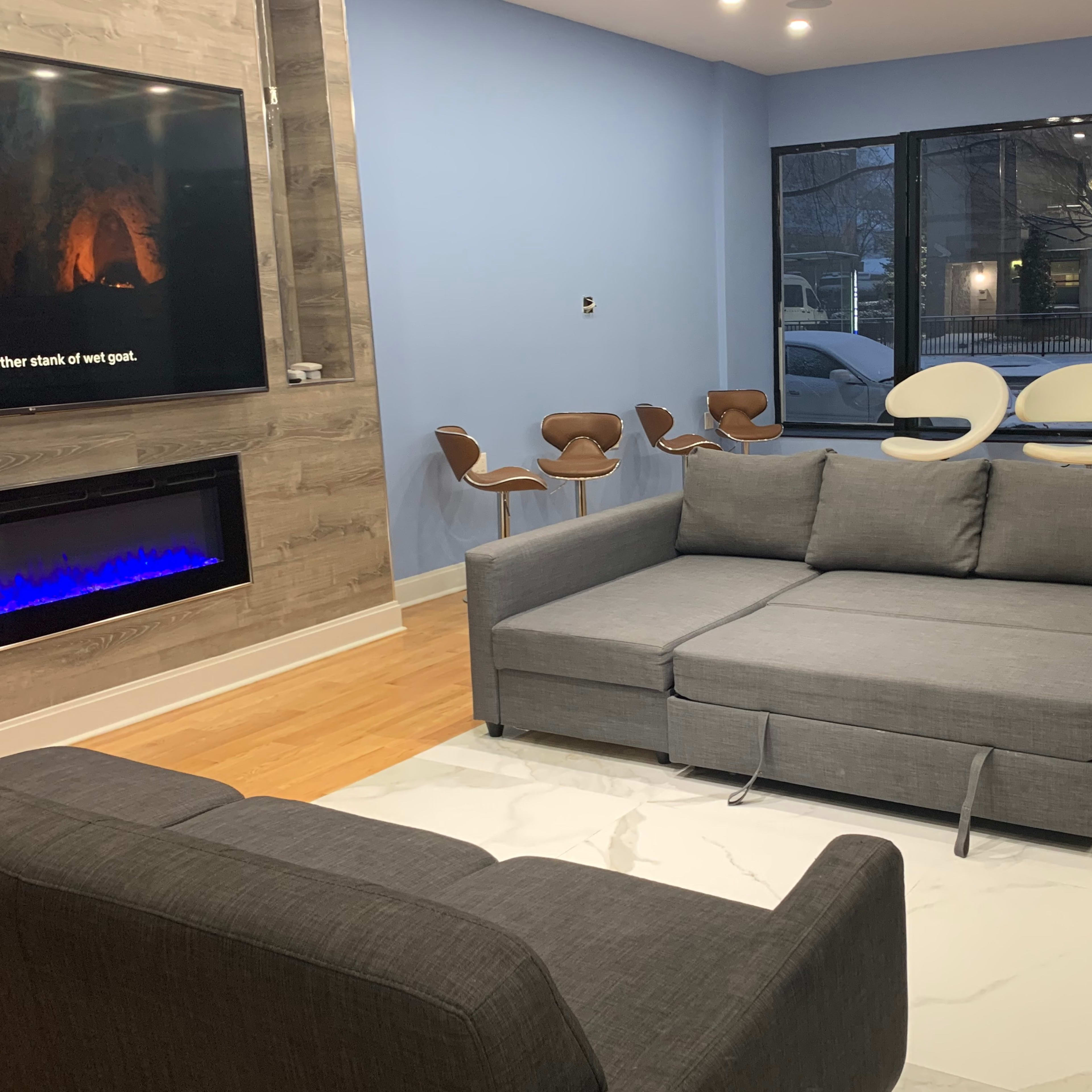 A modern living room with a gray sectional sofa, a white rug, and a set of stylish chairs near a large window.