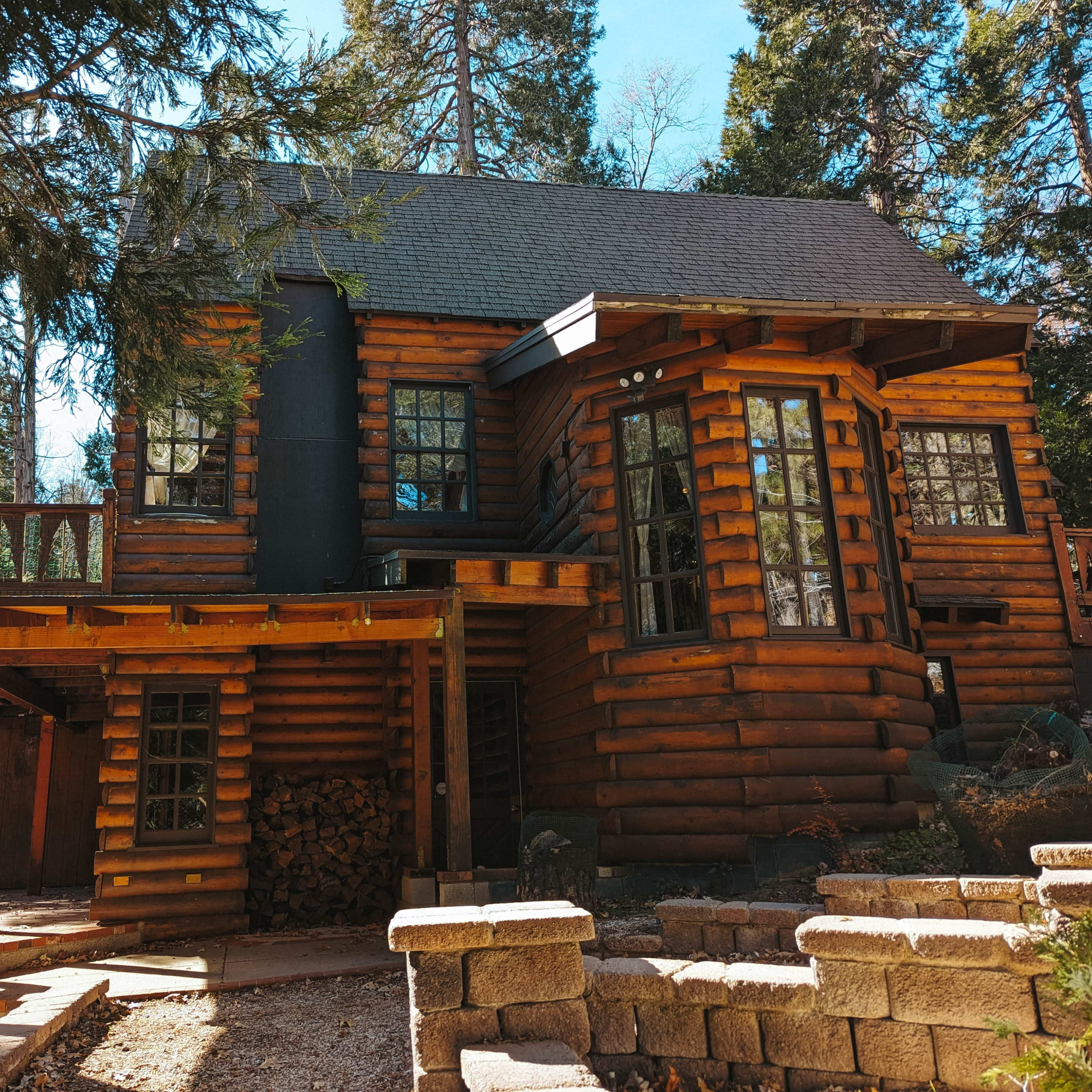 A log cabin with multiple windows and a deck is set among tall trees.