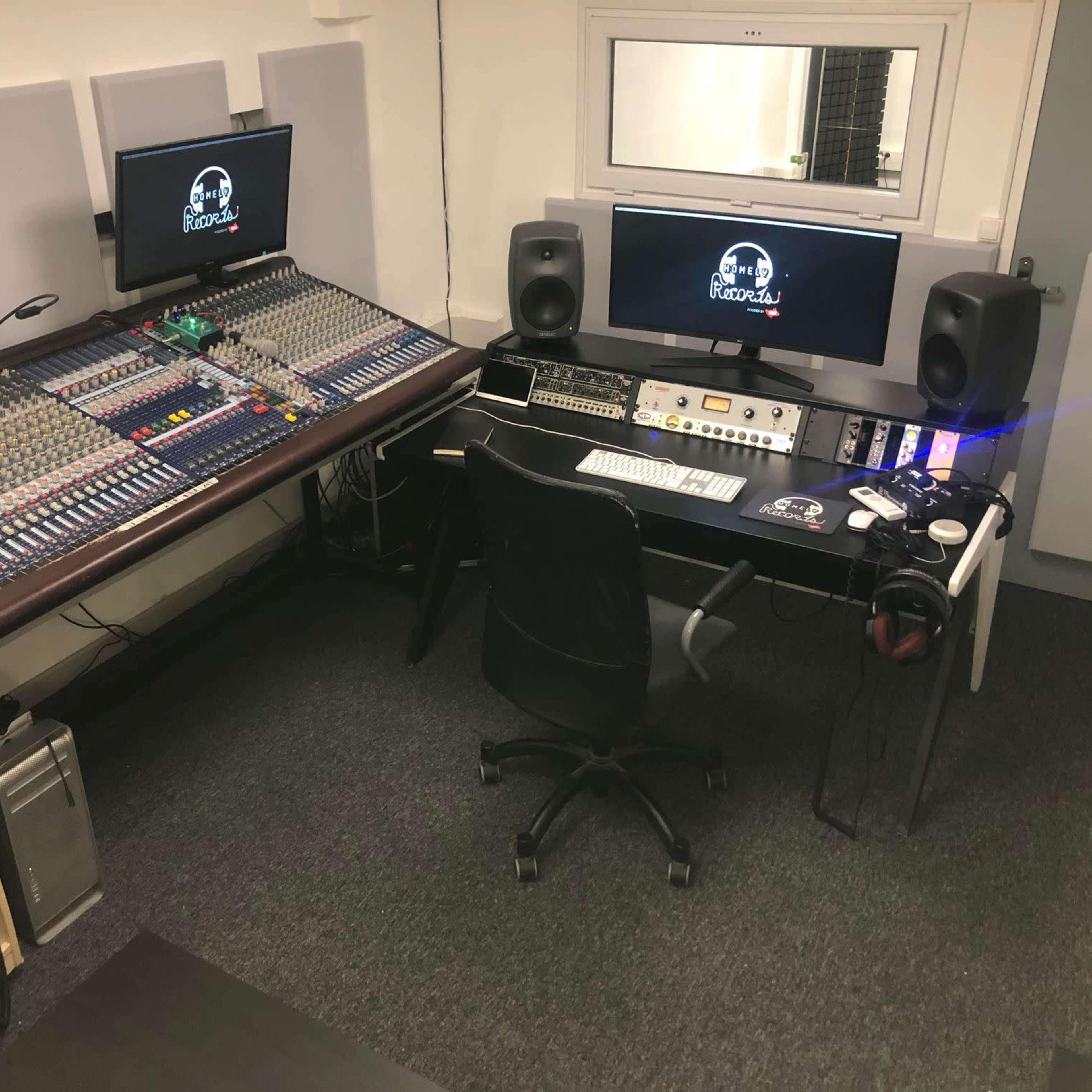A modern audio recording studio featuring a large mixer, computer monitors, and various audio equipment.