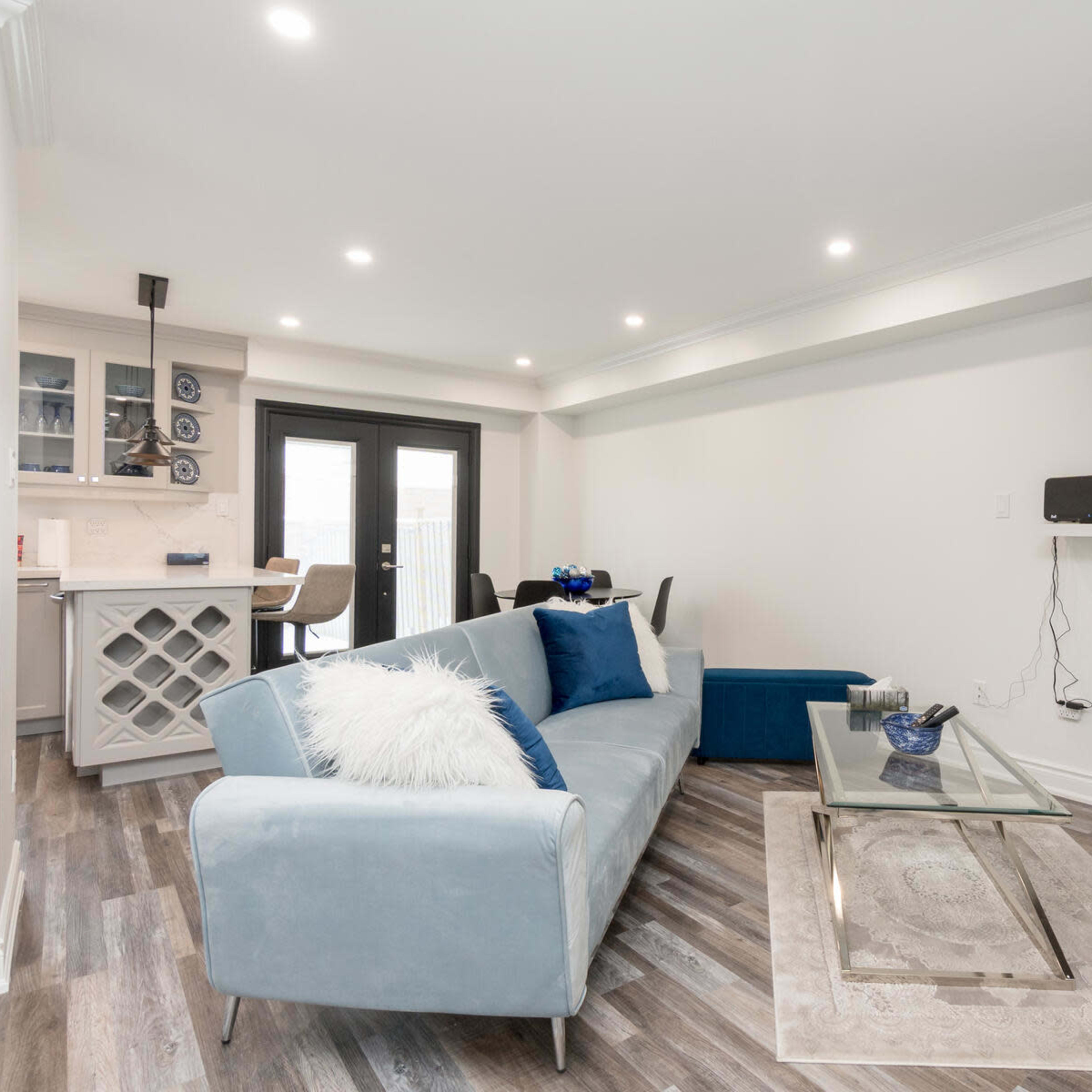 A modern living room featuring a light blue sofa, a glass coffee table, an electric fireplace with a marbled wall, and a mounted television.