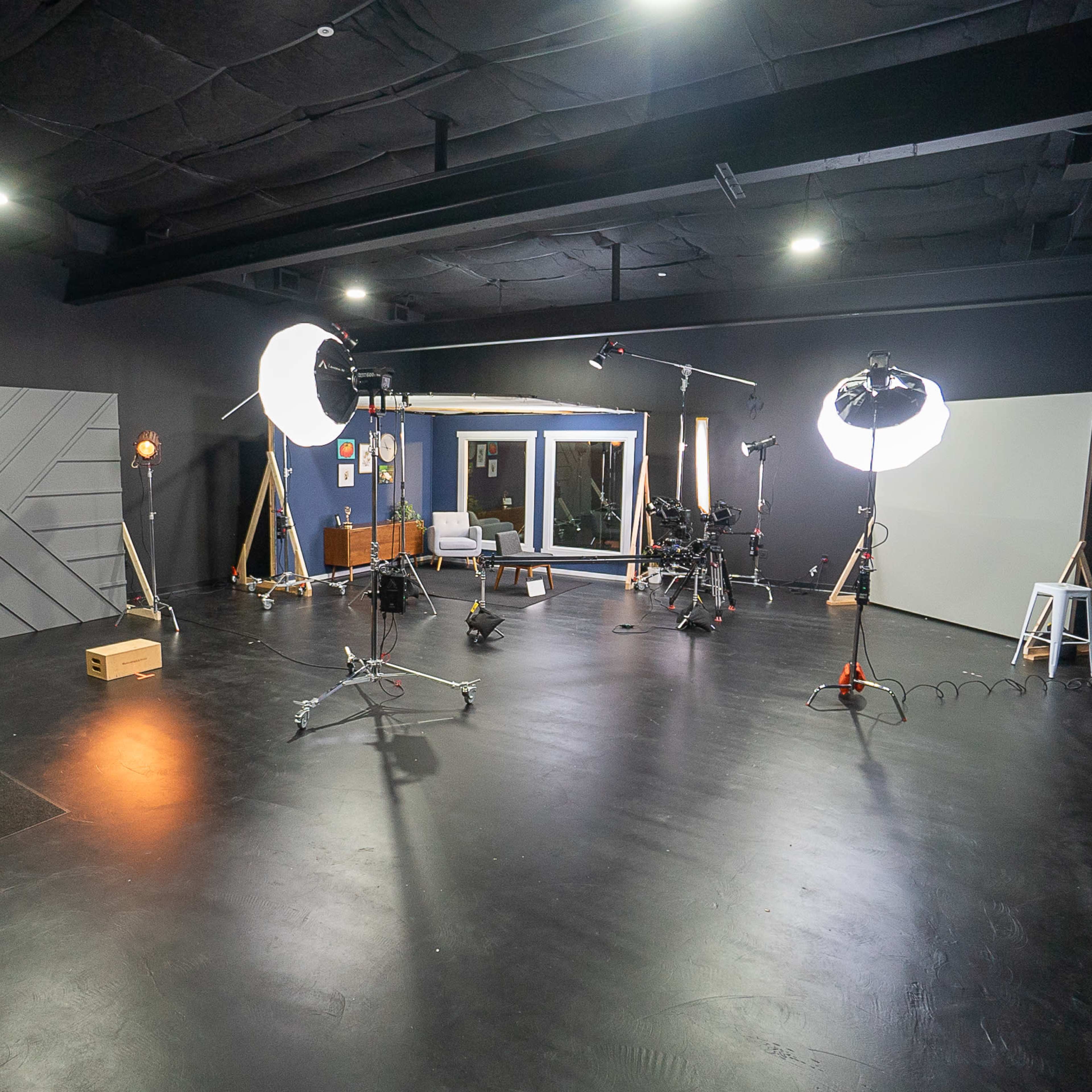 A dimly lit photography studio features various lighting equipment, a camera on a tripod, and a white backdrop.