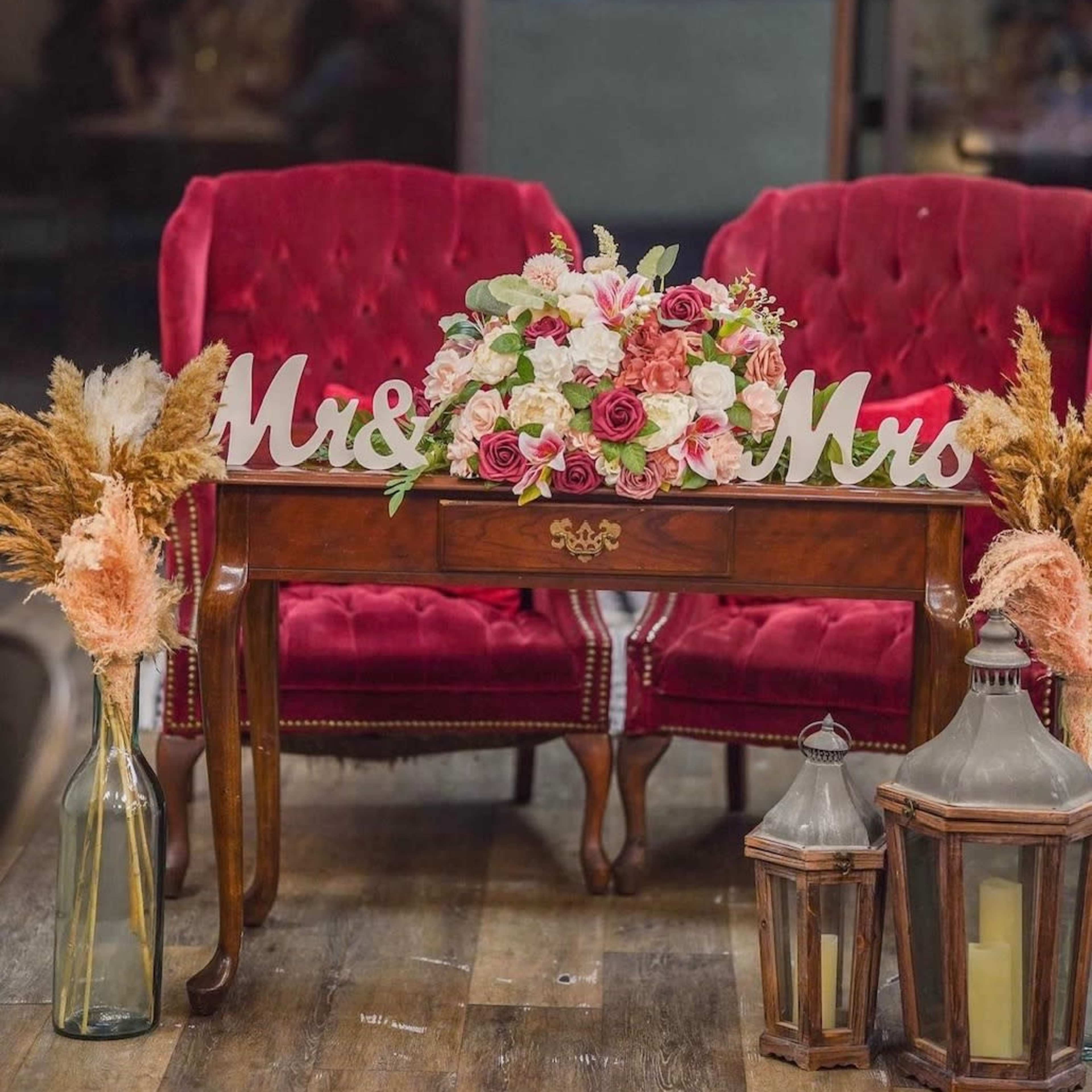 A cozy seating area with two red velvet chairs, a wooden table adorned with a flower bouquet, and decorative lanterns.
