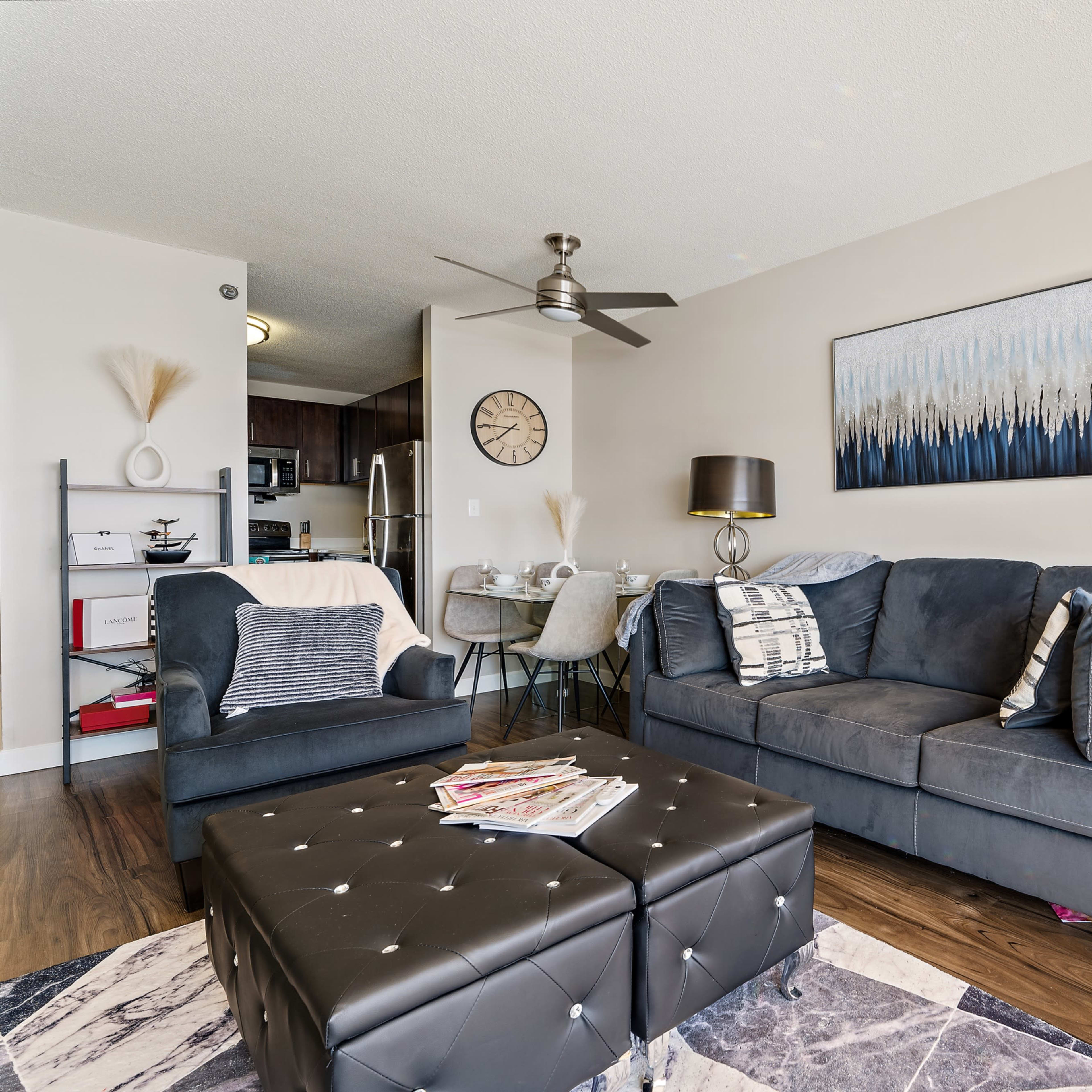 The living area features a dark sofa, two lamps, a coffee table with magazines, and a dining space with a round table in the background.