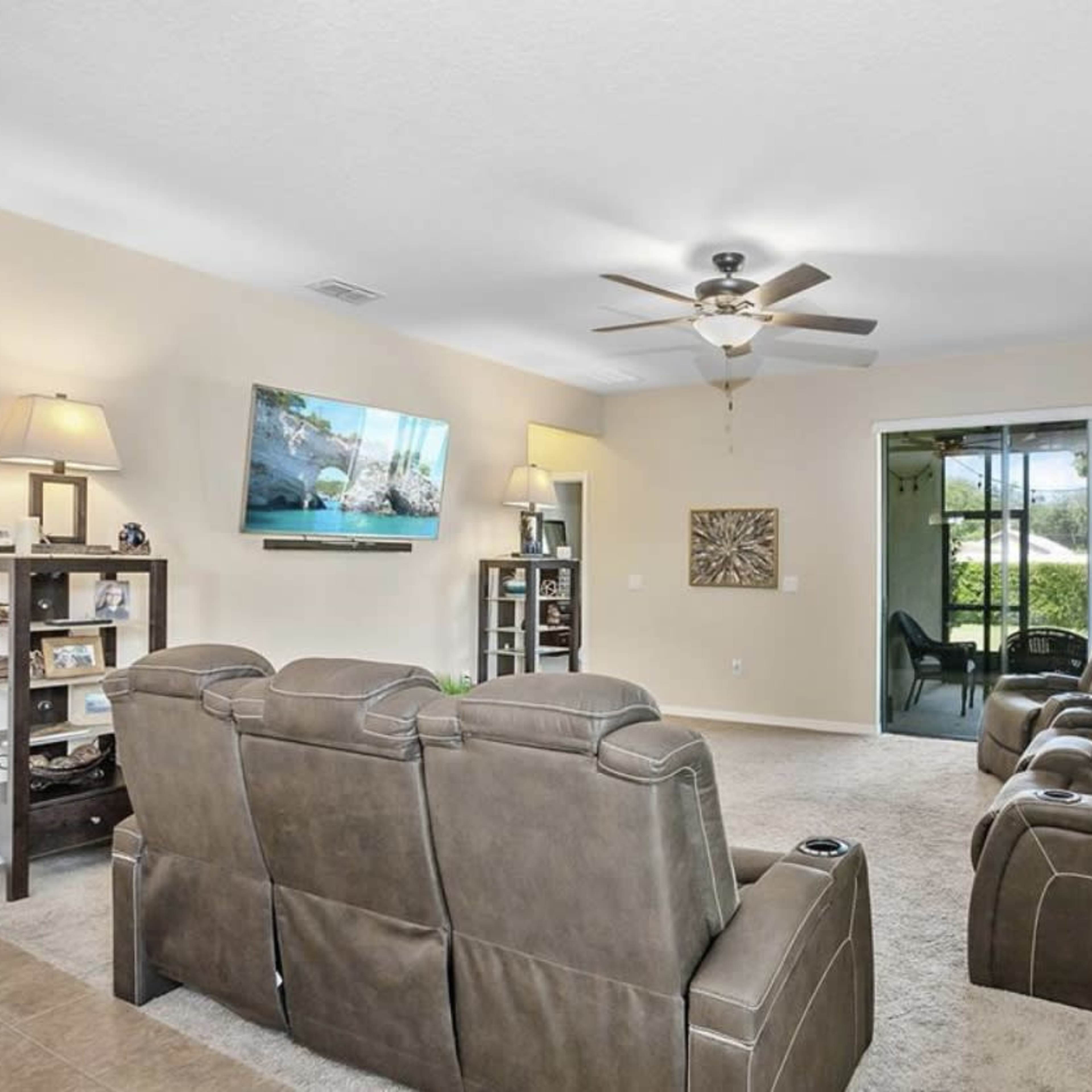The living room features a set of brown reclining chairs, a wall-mounted television, and a sliding glass door leading to an outdoor space.