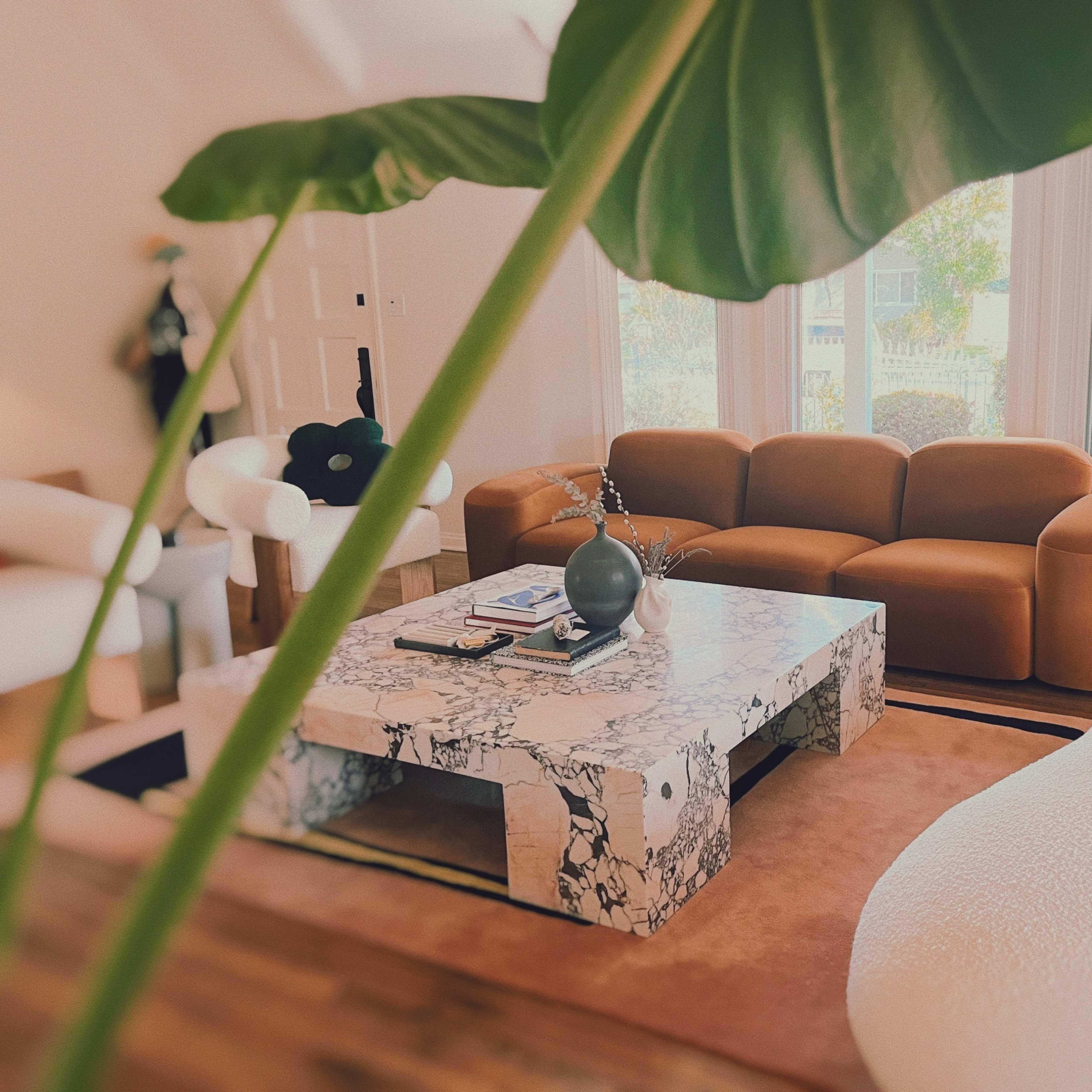 A modern living room featuring a brown sofa, a marble coffee table, and a curved white chair, surrounded by natural light.