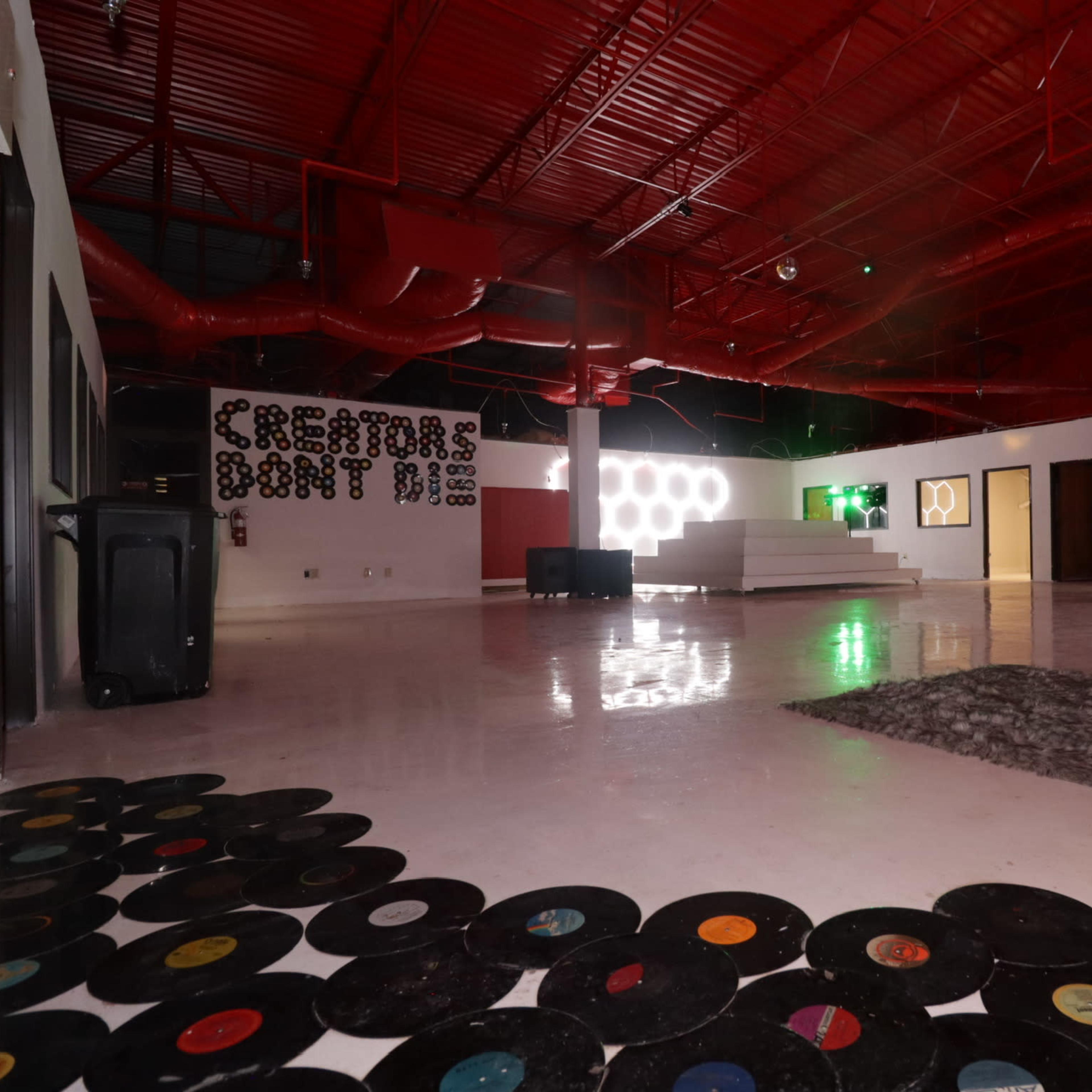 A spacious room with a red ceiling, white floor, and decorative vinyl records spread across the floor, featuring a wall that reads "CREATORS DONT FLY."