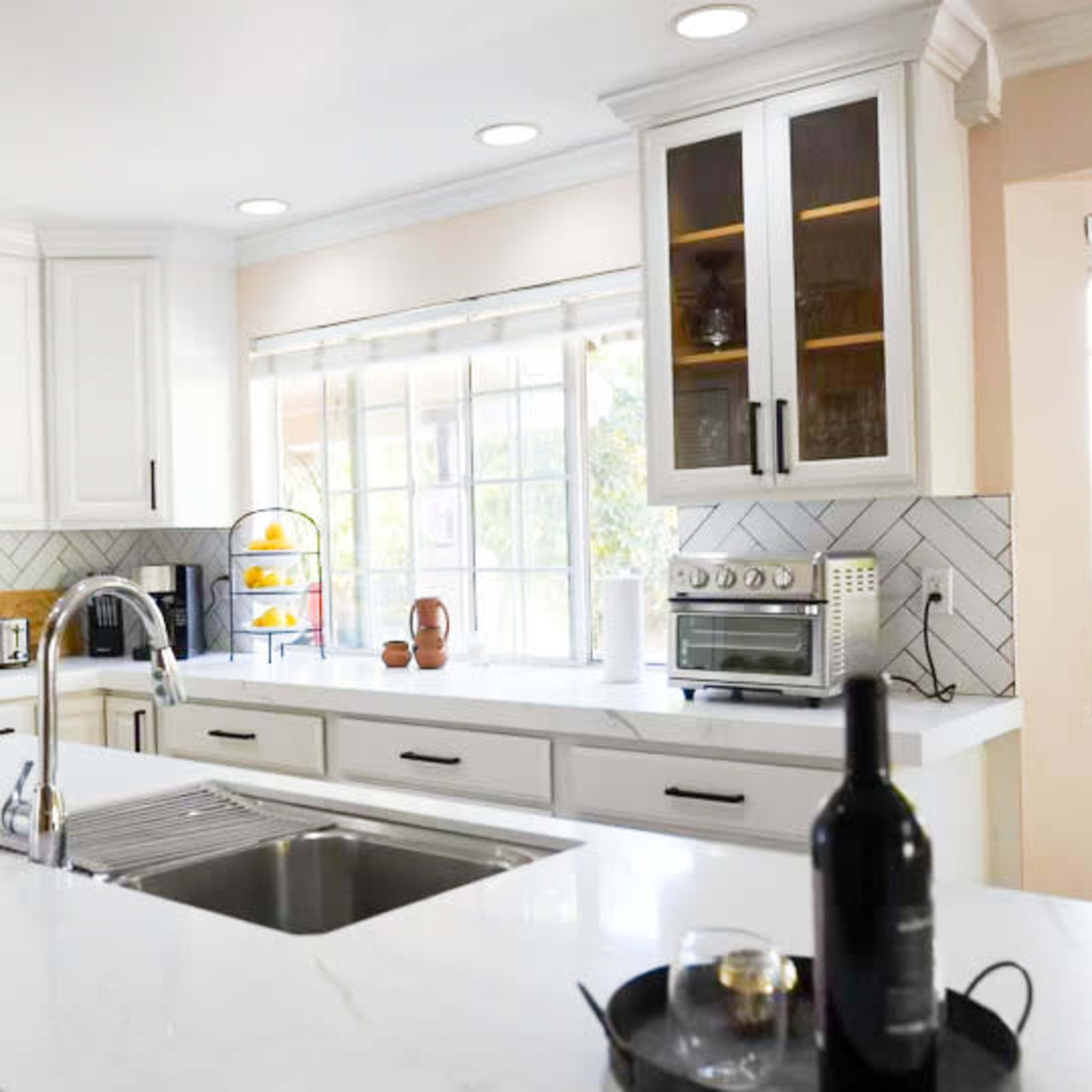 A modern kitchen with white cabinetry, a large island with a sink, and a herringbone-patterned backsplash.