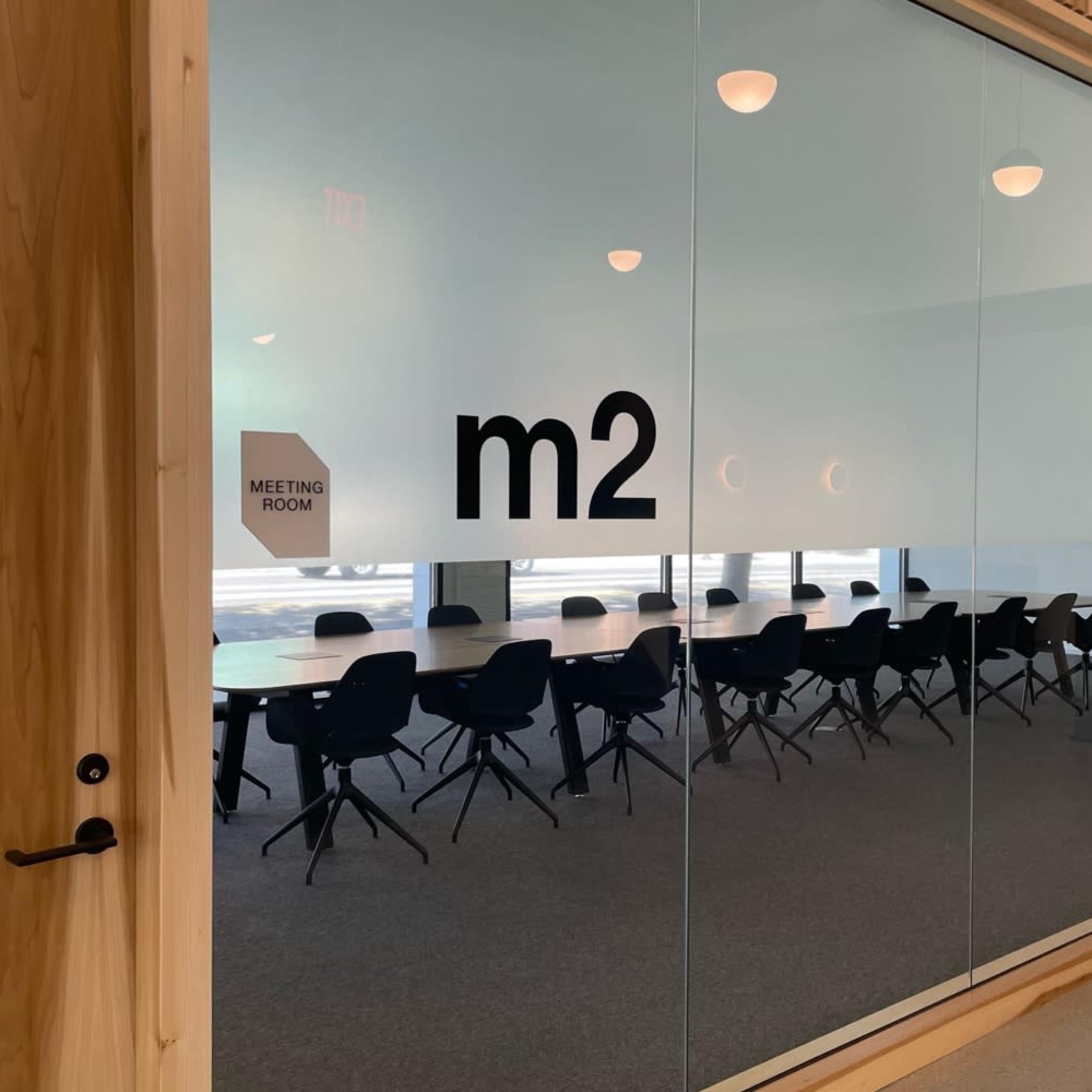 A meeting room labeled "m2" is visible through a glass wall, featuring a long table surrounded by black chairs.