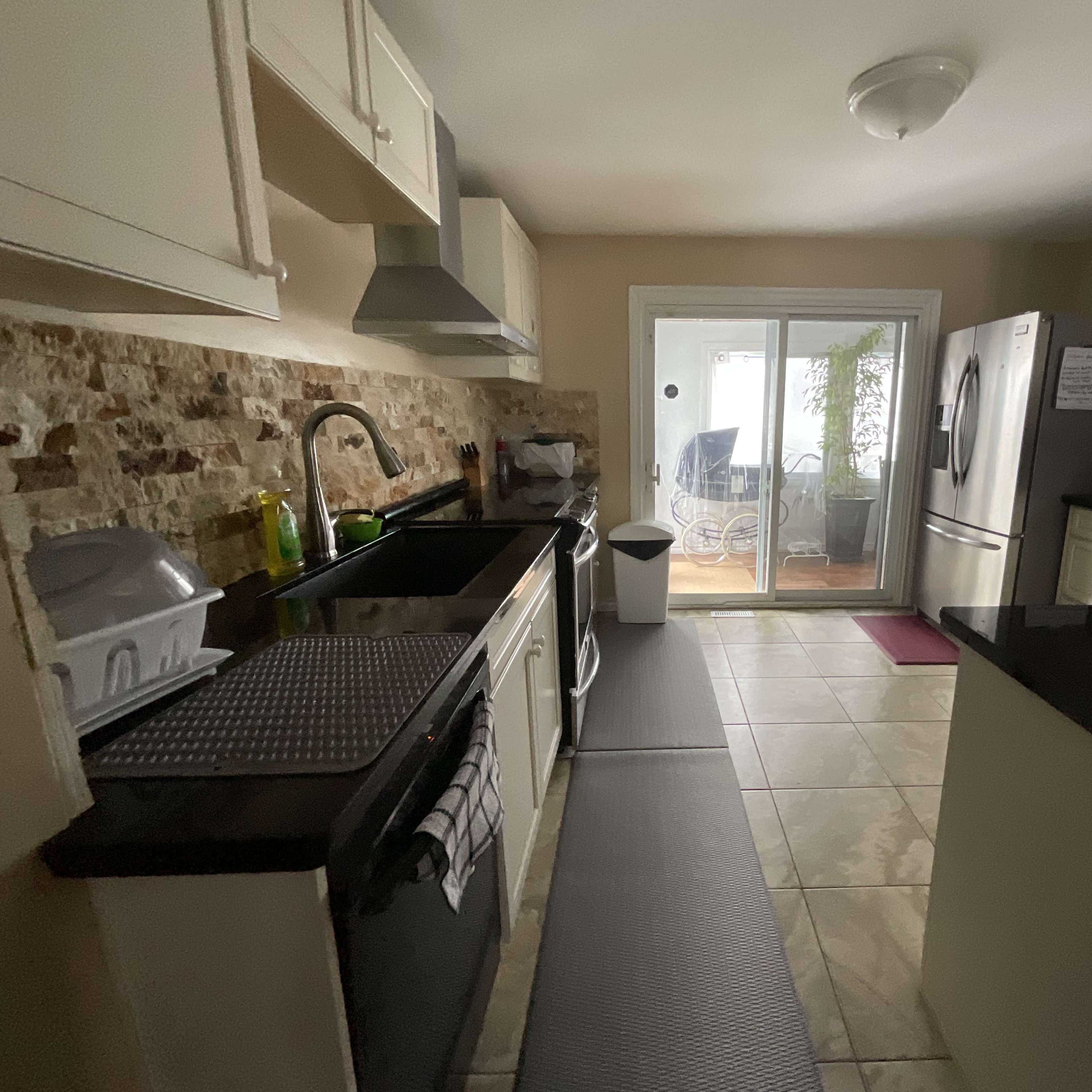 A kitchen with white cabinets, a black countertop, and stainless steel appliances, leading to a glass sliding door that opens to a porch area.