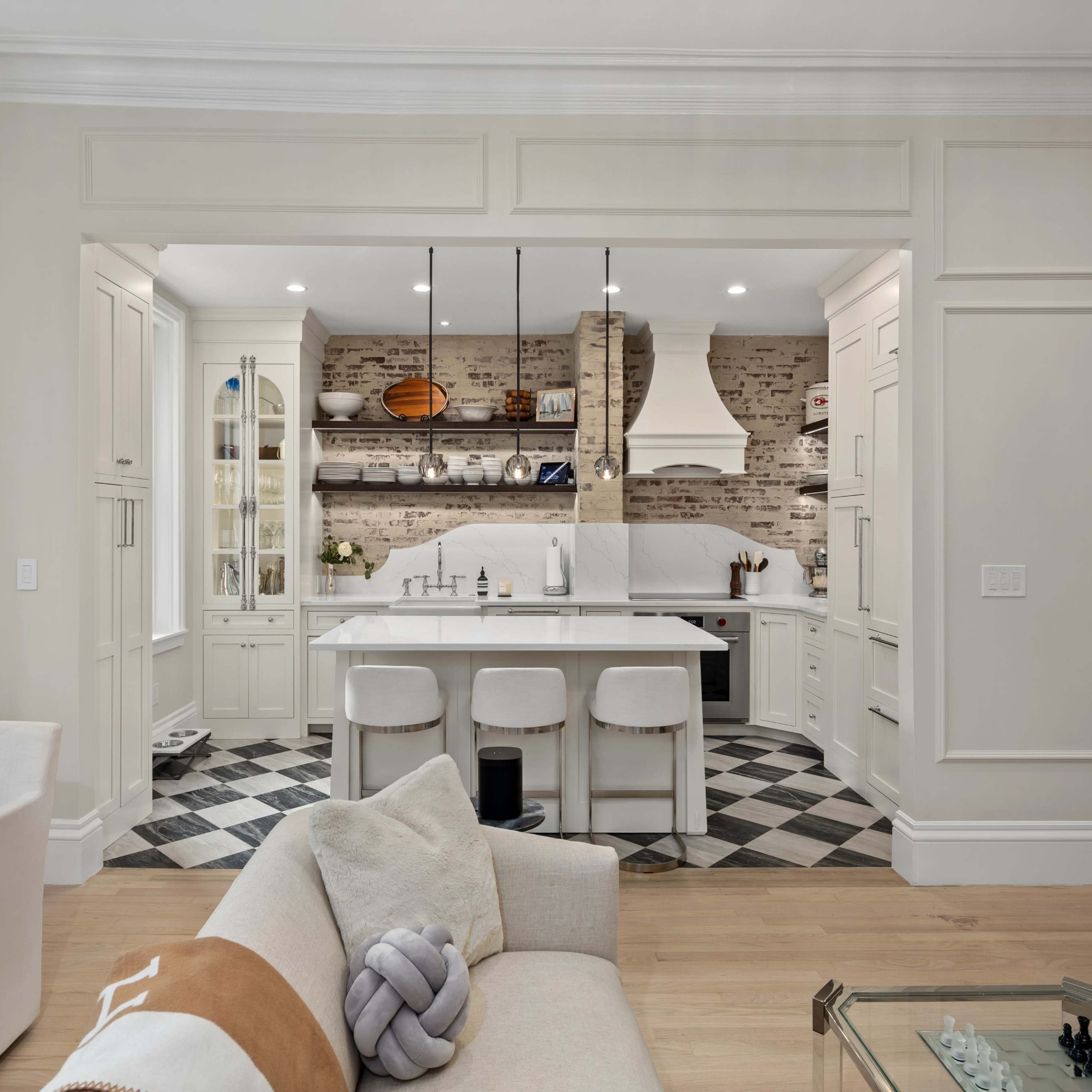 A modern kitchen features a large island with bar stools, surrounded by light-colored cabinetry and a brick backsplash.