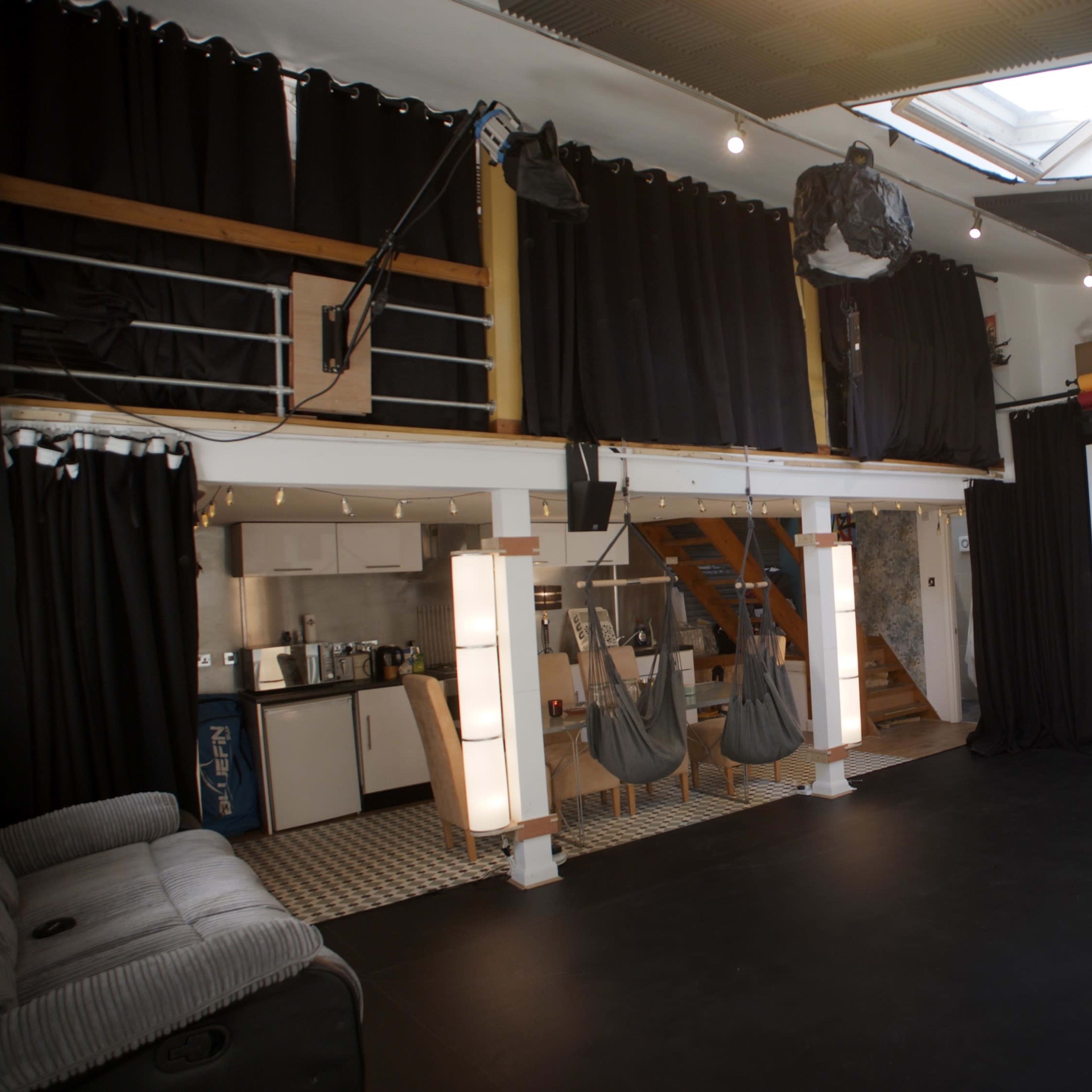 A spacious interior room with a black floor, wooden stairs leading to an upper level, and a large projection screen against one wall.