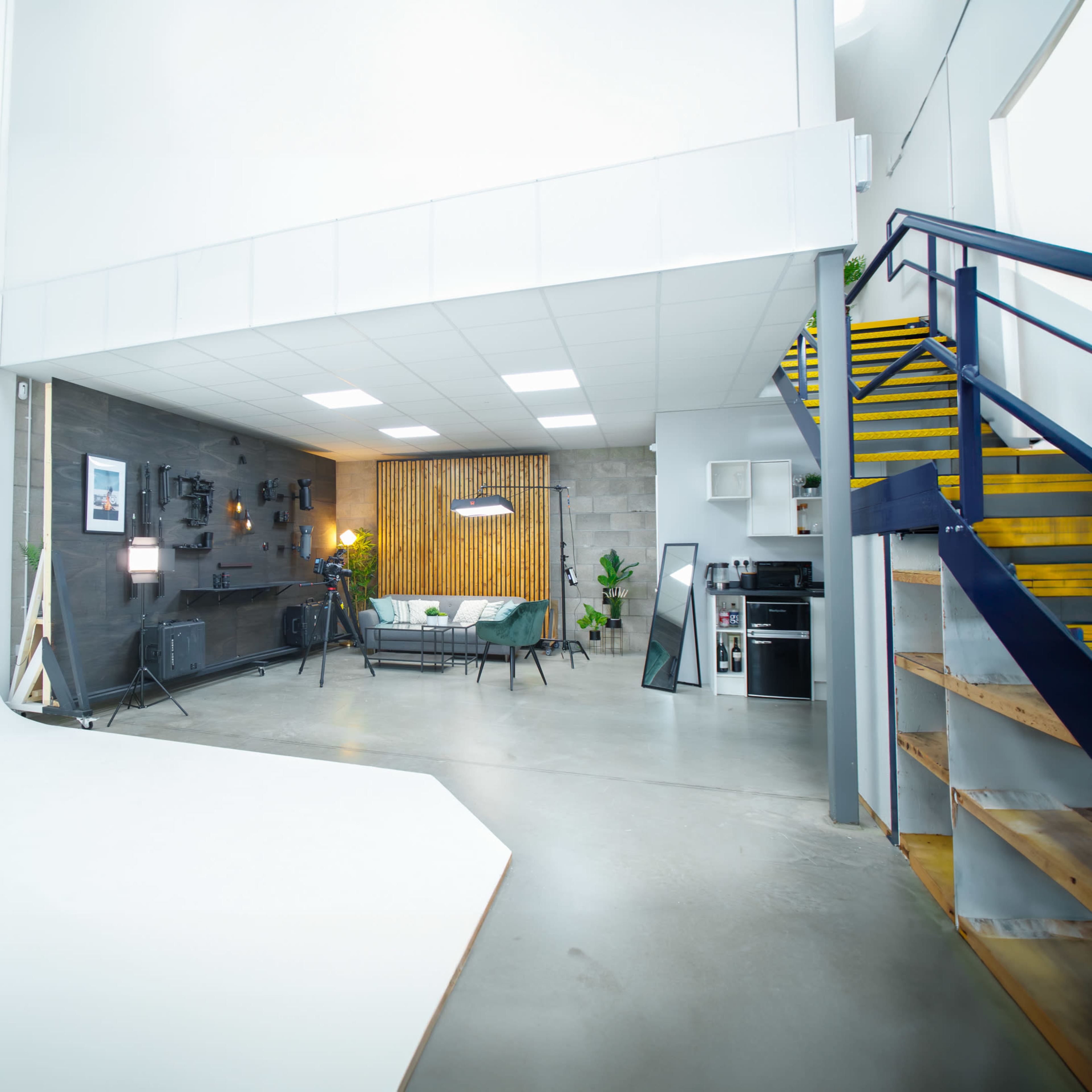 A modern, open studio space with a gray wall, wooden accents, seating area, and stairs leading to an upper level.