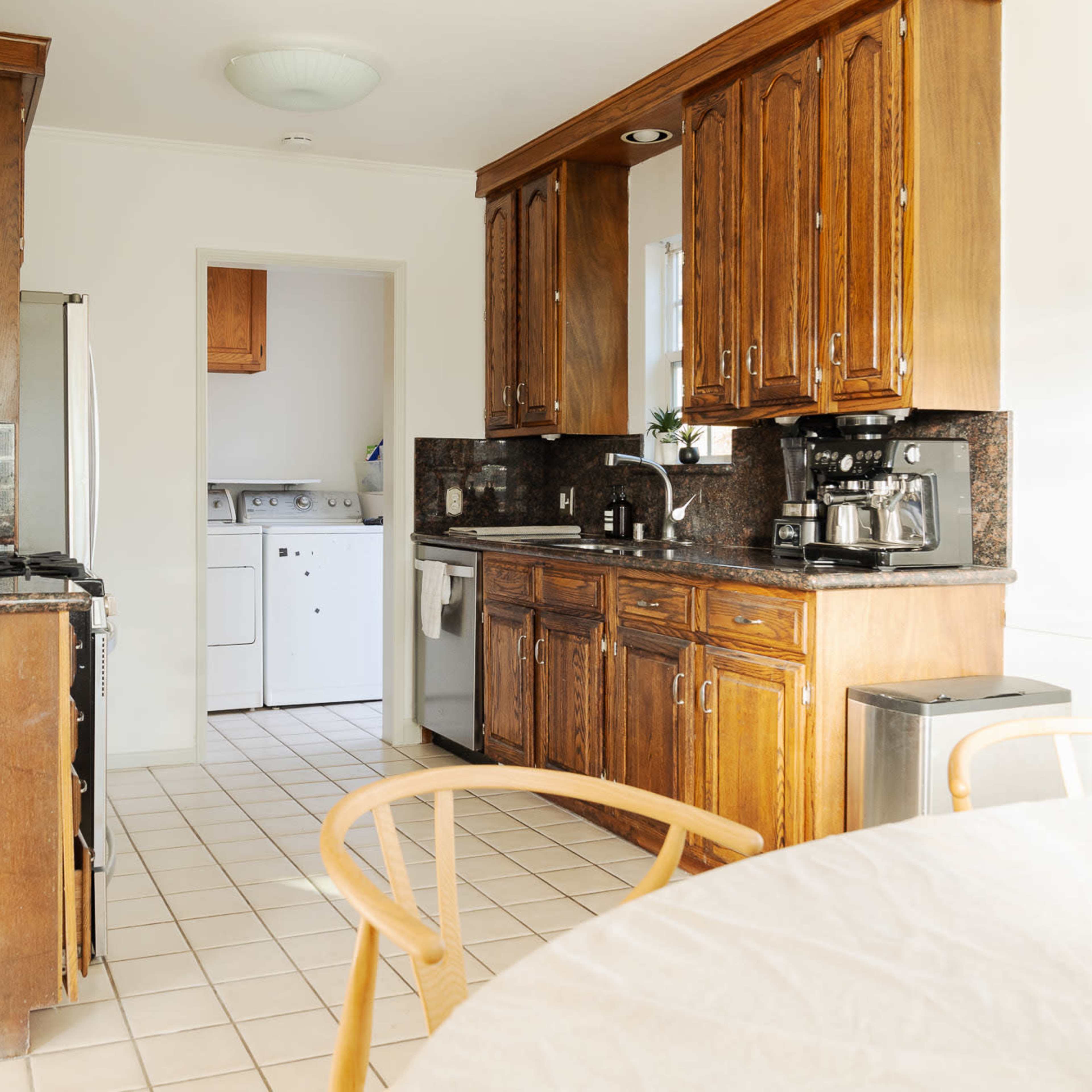 A kitchen features wooden cabinets, a gas stove, and a small dining table, with a view into a laundry area at the back.