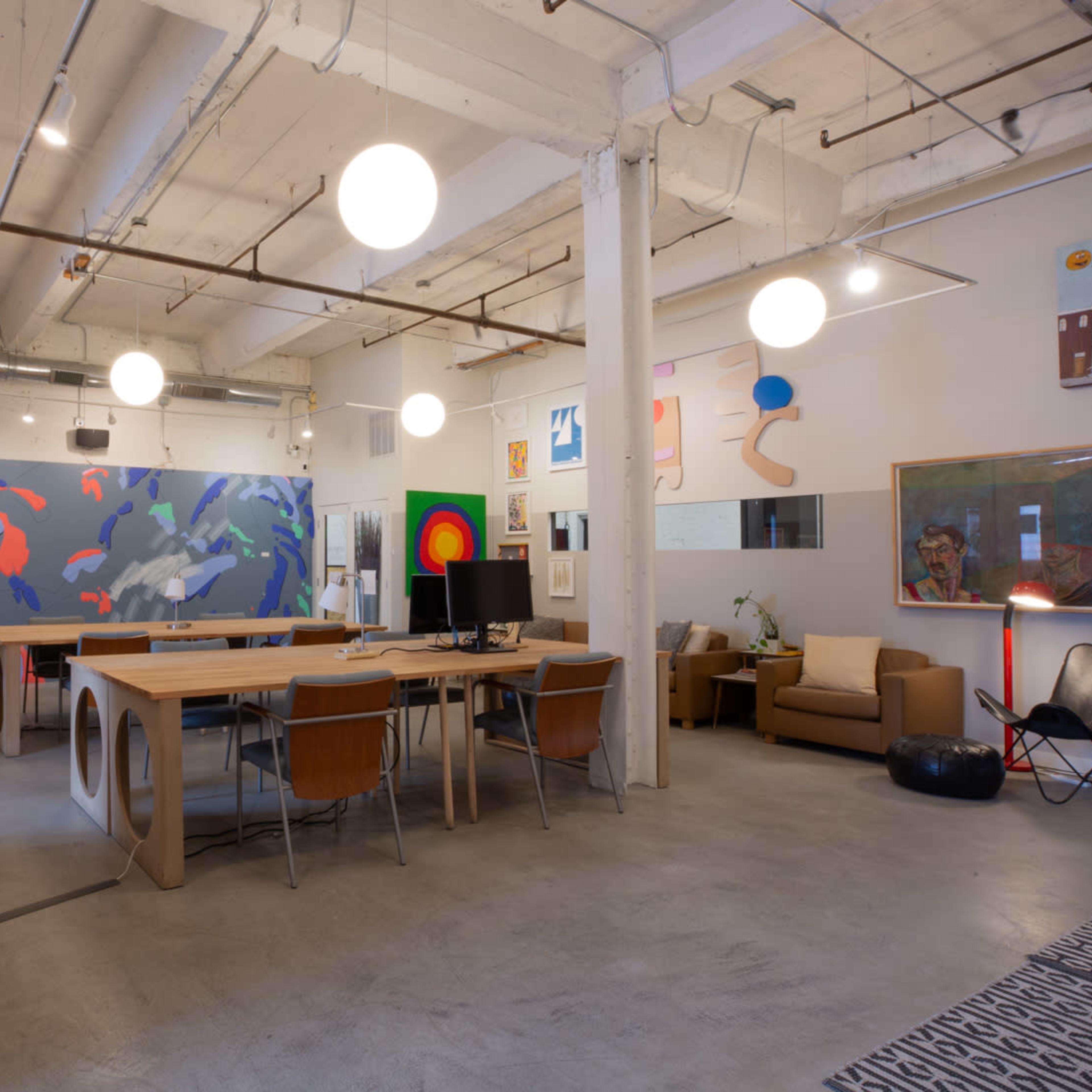 A spacious office area with a long wooden table, comfortable seating, and colorful wall art.