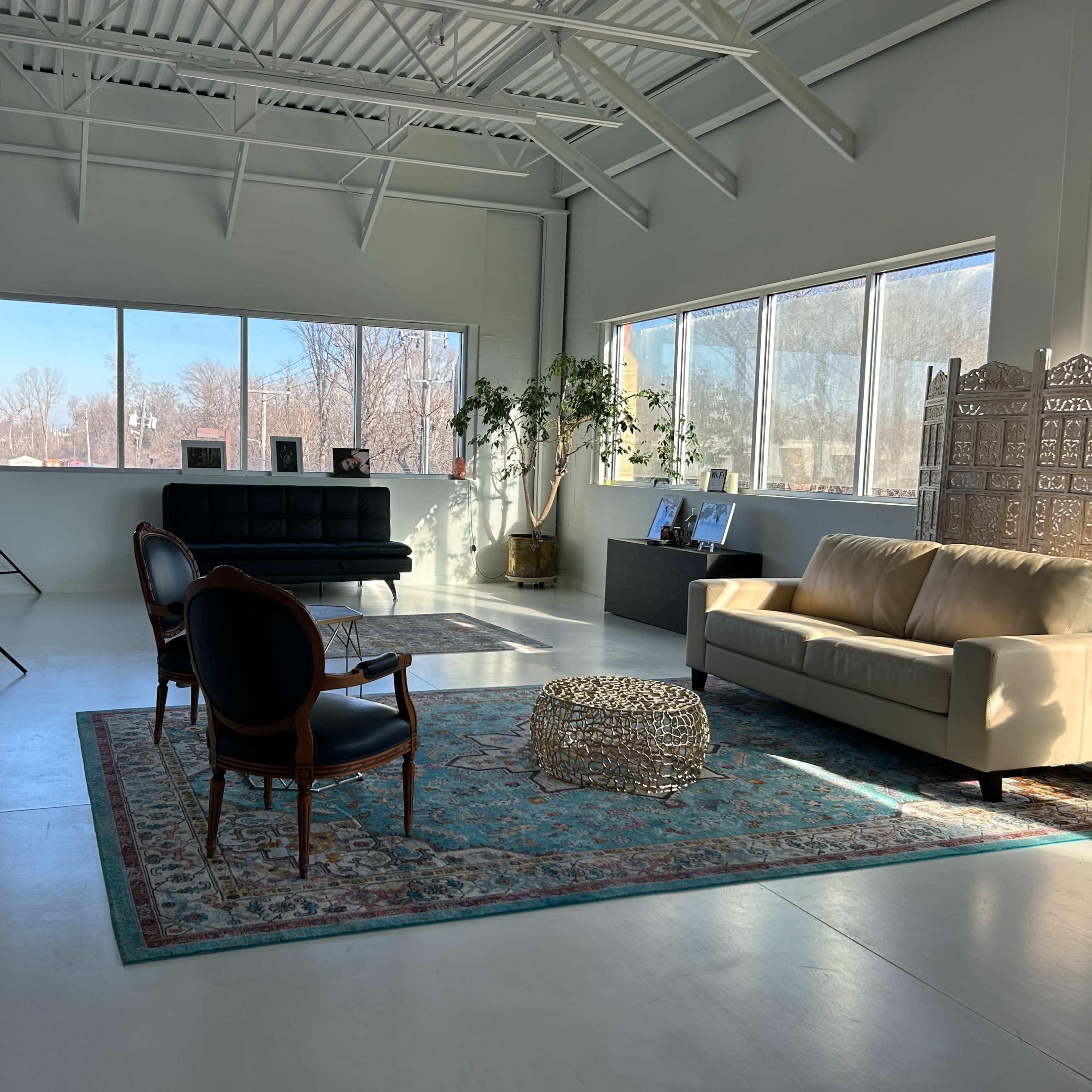 A bright, modern interior space with a black sofa, a beige couch, and large windows letting in natural light.